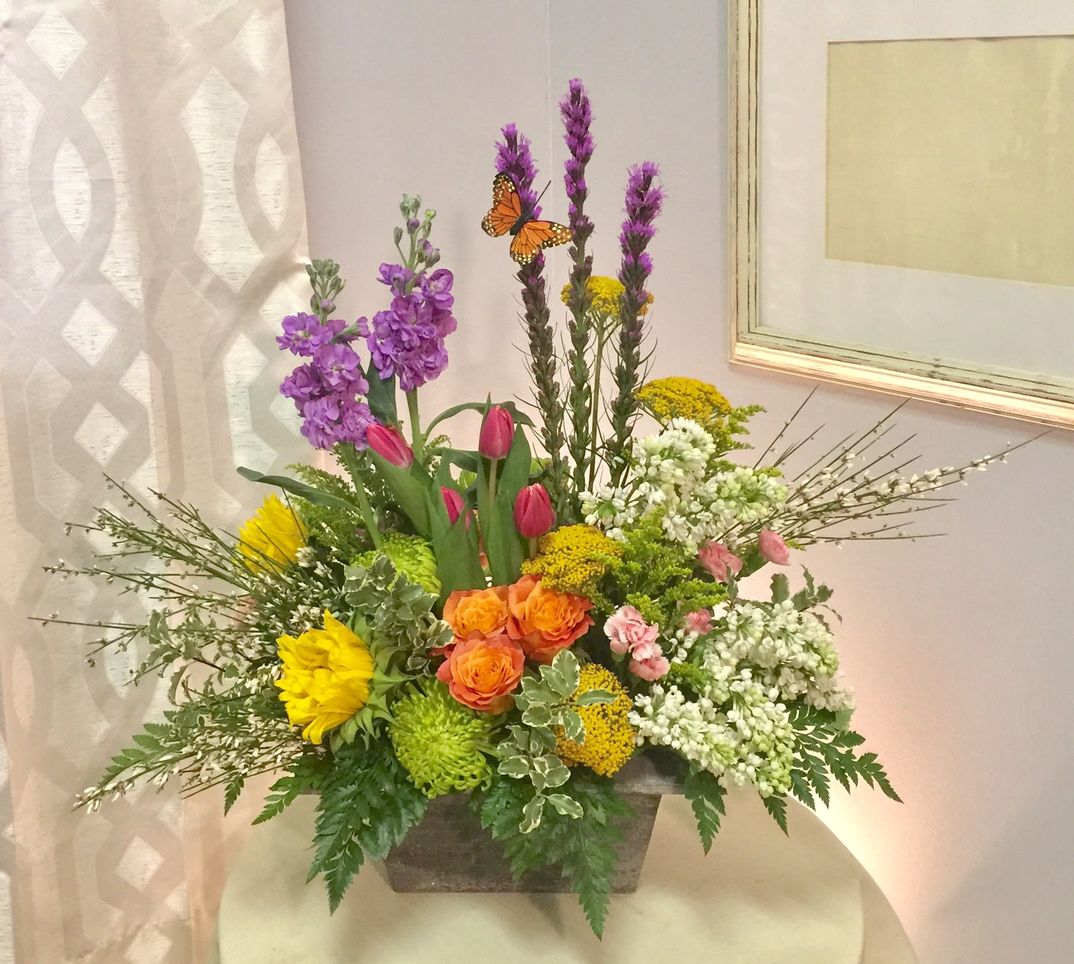Mixed floral arrangement in a rectangular container with purple, yellow, orange, pink, and white blooms