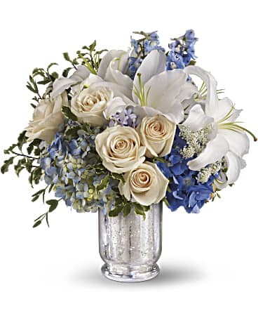 Teleflora's Seaside Centerpiece - Having a beach wedding or beach themed celebration? This beautiful centerpiece captures the wonder and romance of the seaside, making it a perfect choice for beach wedding flowers. Beautiful blue hydrangea, delphinium, crème roses and more are perfectly arranged in a divine Mercury Glass Vase. These wonderful beach themed flowers are so pretty, there's no doubt it will be love at first sight.