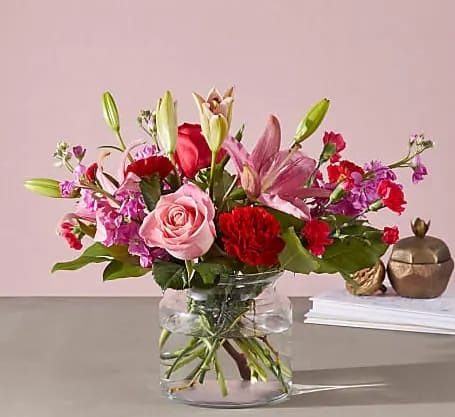 Mixed pink and red flowers arranged in a clear glass vase