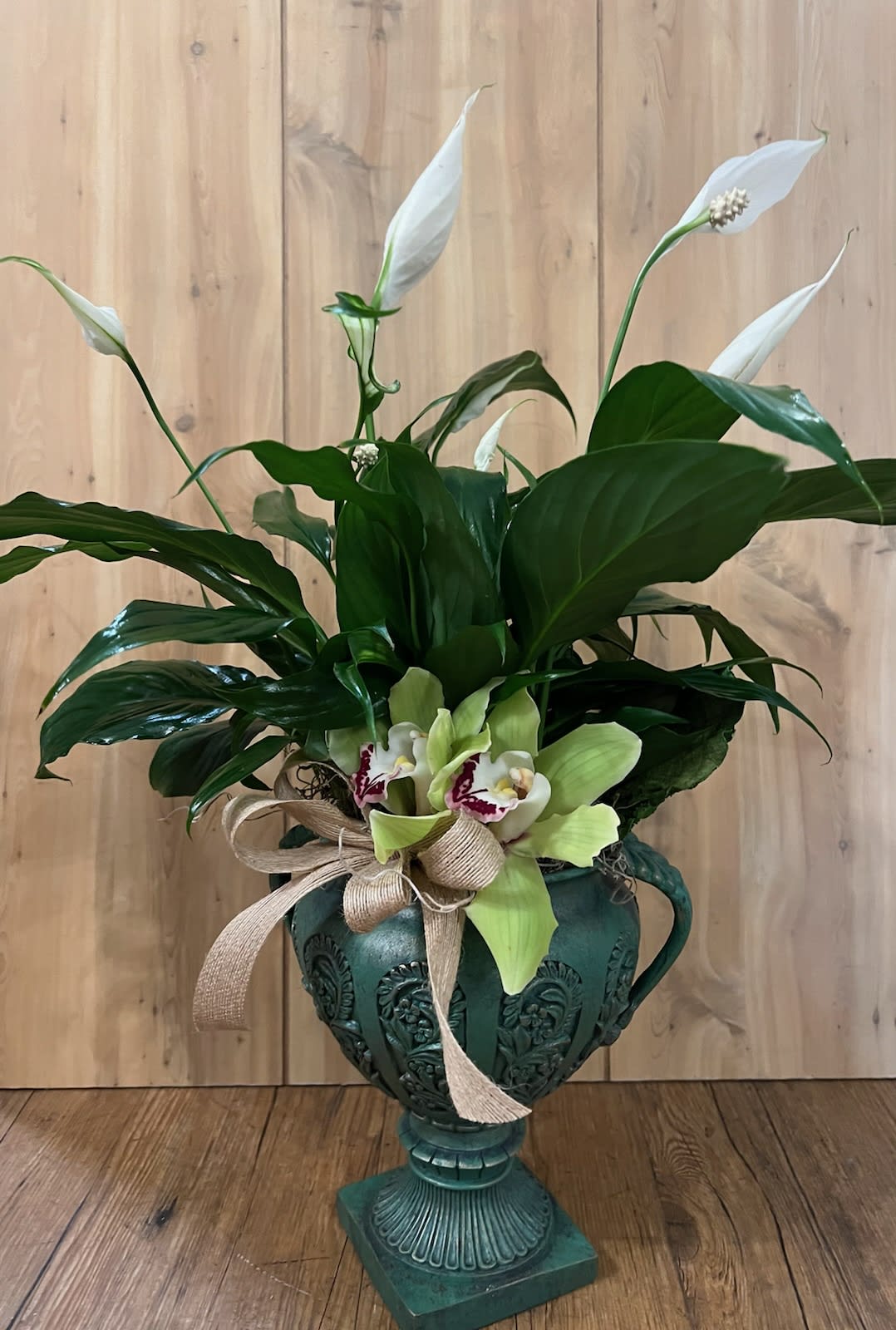 White peace lilies and orchids in a decorative green urn