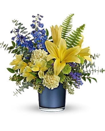 SAPPHIRE SUNRISE - Bright yellow lilies and roses burst against tall sapphire-blue delphinium in this yellow, blue, white, and green floral arrangement-an uplifting everyday bouquet perfect for birthdays, thank-you gifts, or "just because" moments. The strong sunny-and-cool contrast creates an energetic, cheerful impression that will make the person you're thinking of feel seen and celebrated, whether placed on a kitchen table or a workplace desk.  