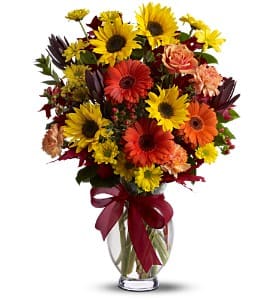 Mixed bouquet of sunflowers, gerbera daisies, and carnations in a glass vase