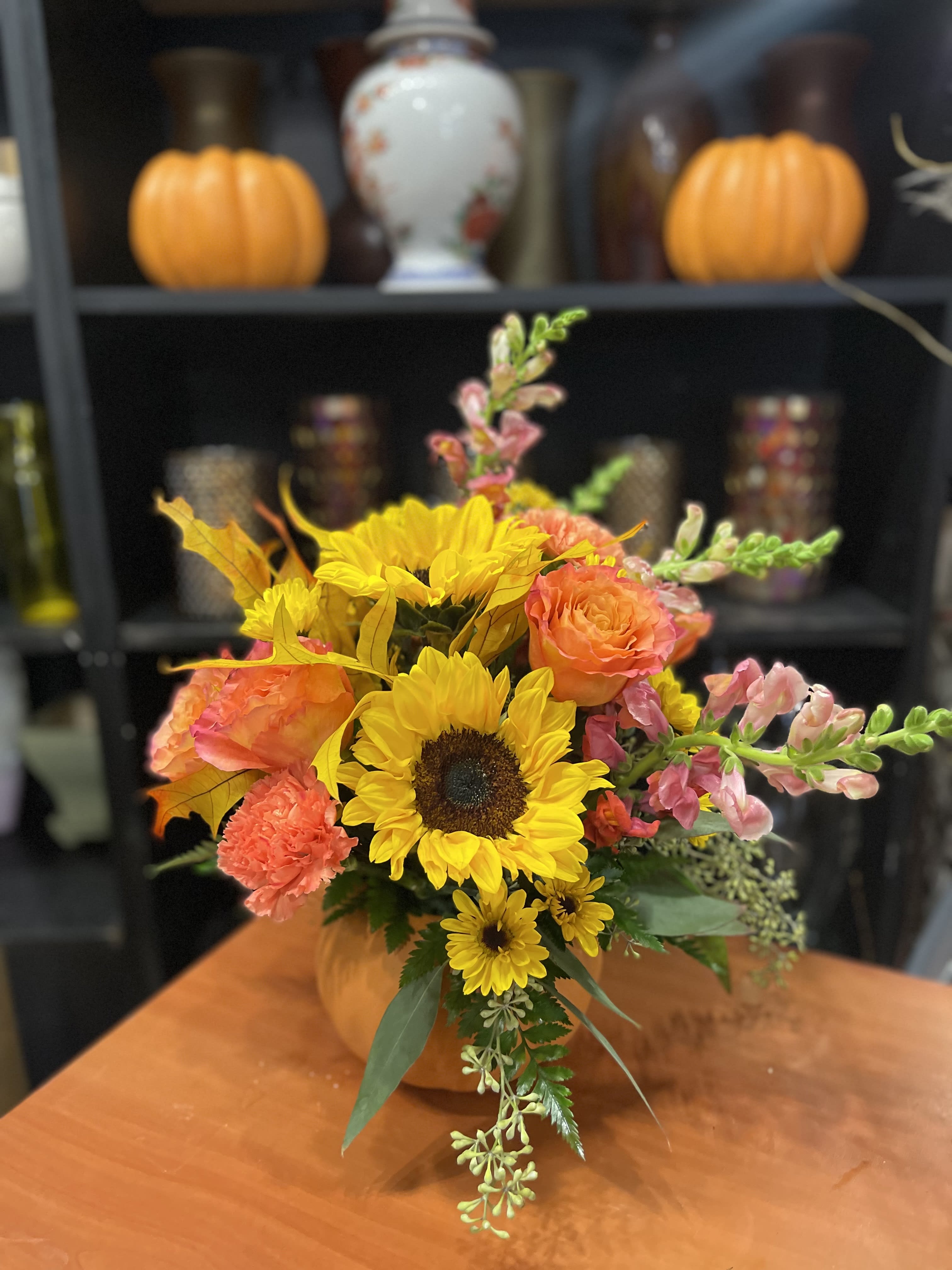 Autumn bouquet with sunflowers, orange roses, and pink snapdragons in a pumpkin vase