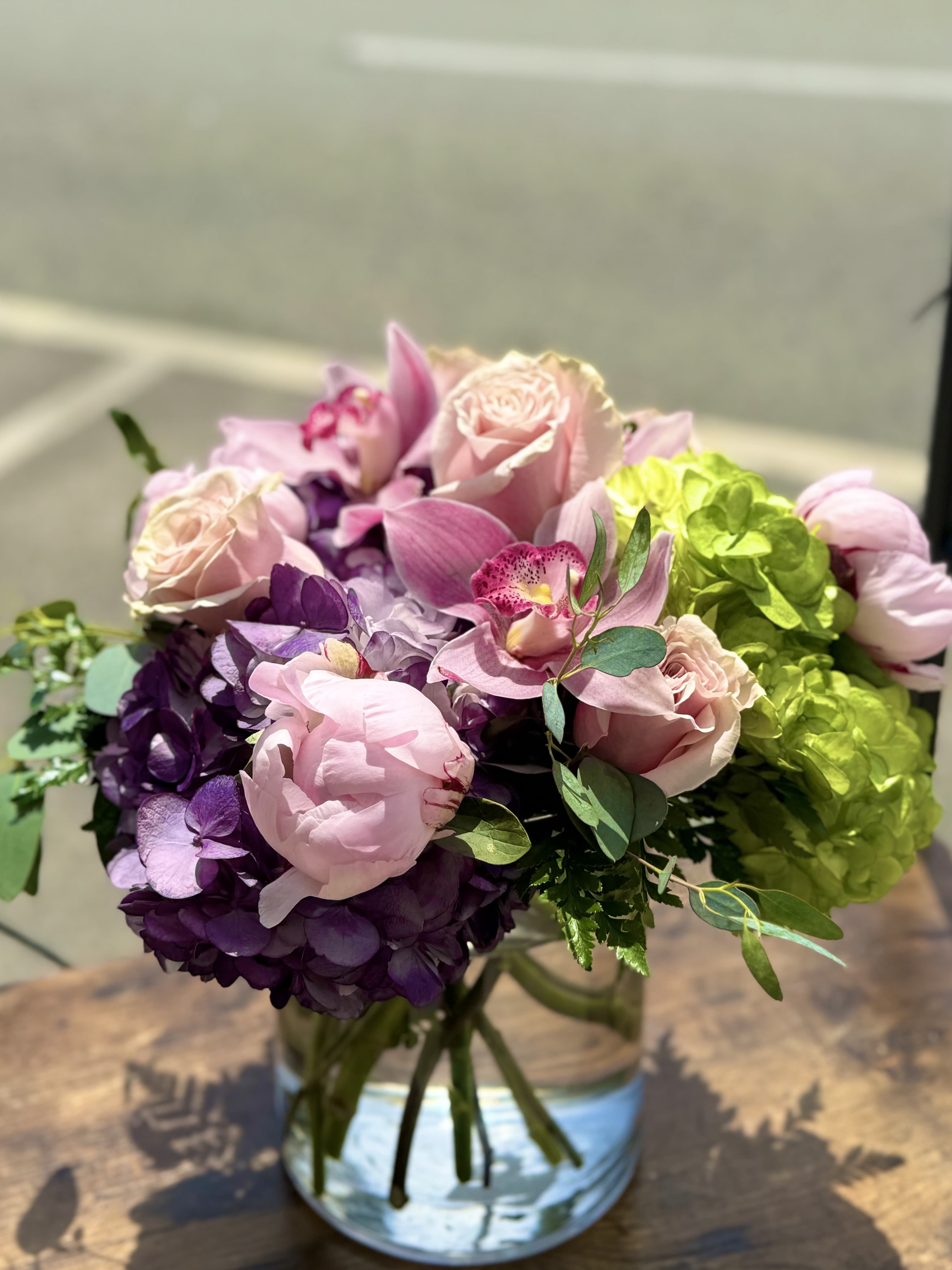 Pink roses and orchids arranged with purple hydrangeas in a glass vase