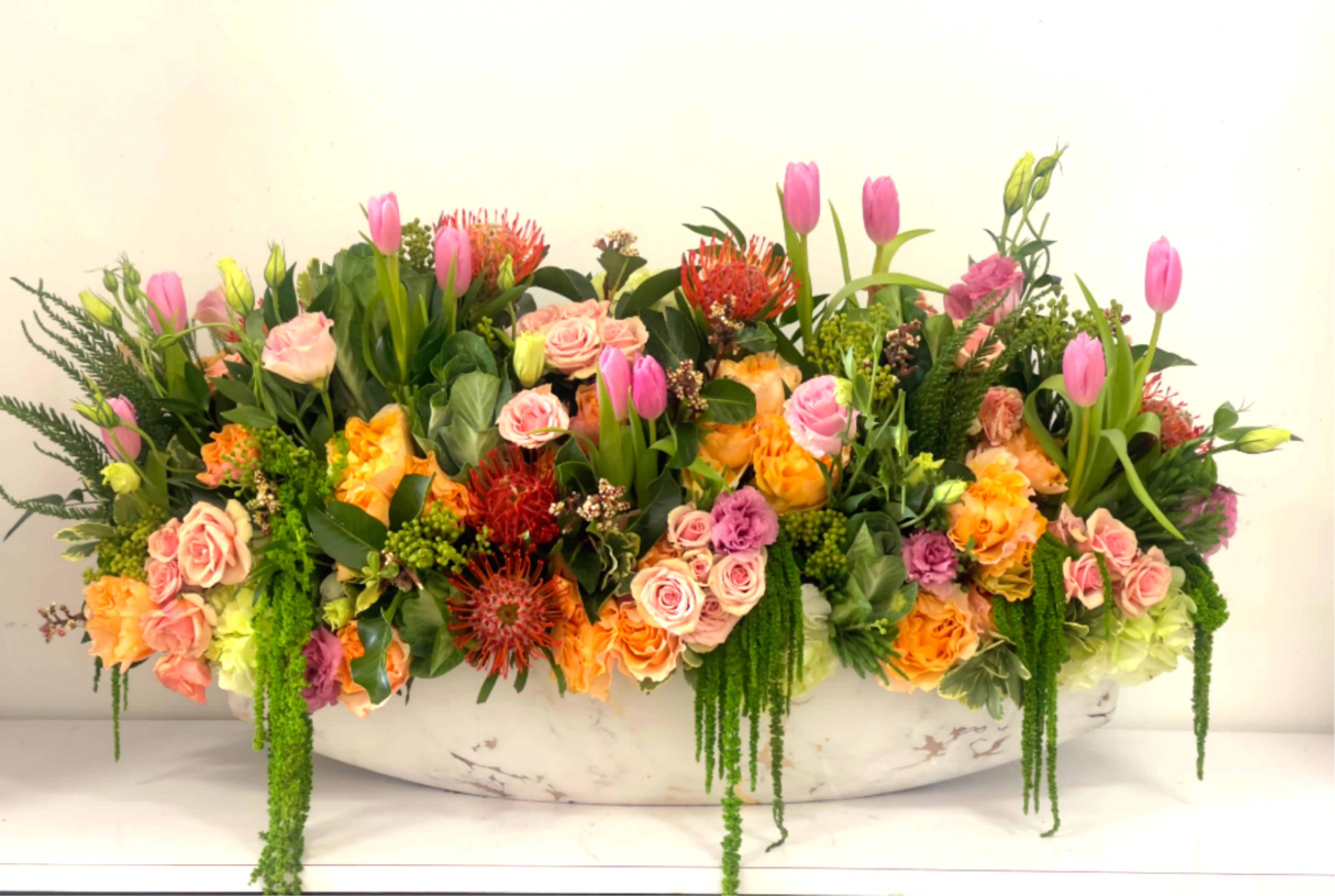 Large mixed floral arrangement with pink tulips and roses in a white bowl