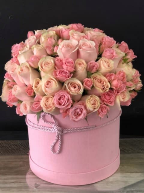 Pink and cream roses arranged in a round pink hat box