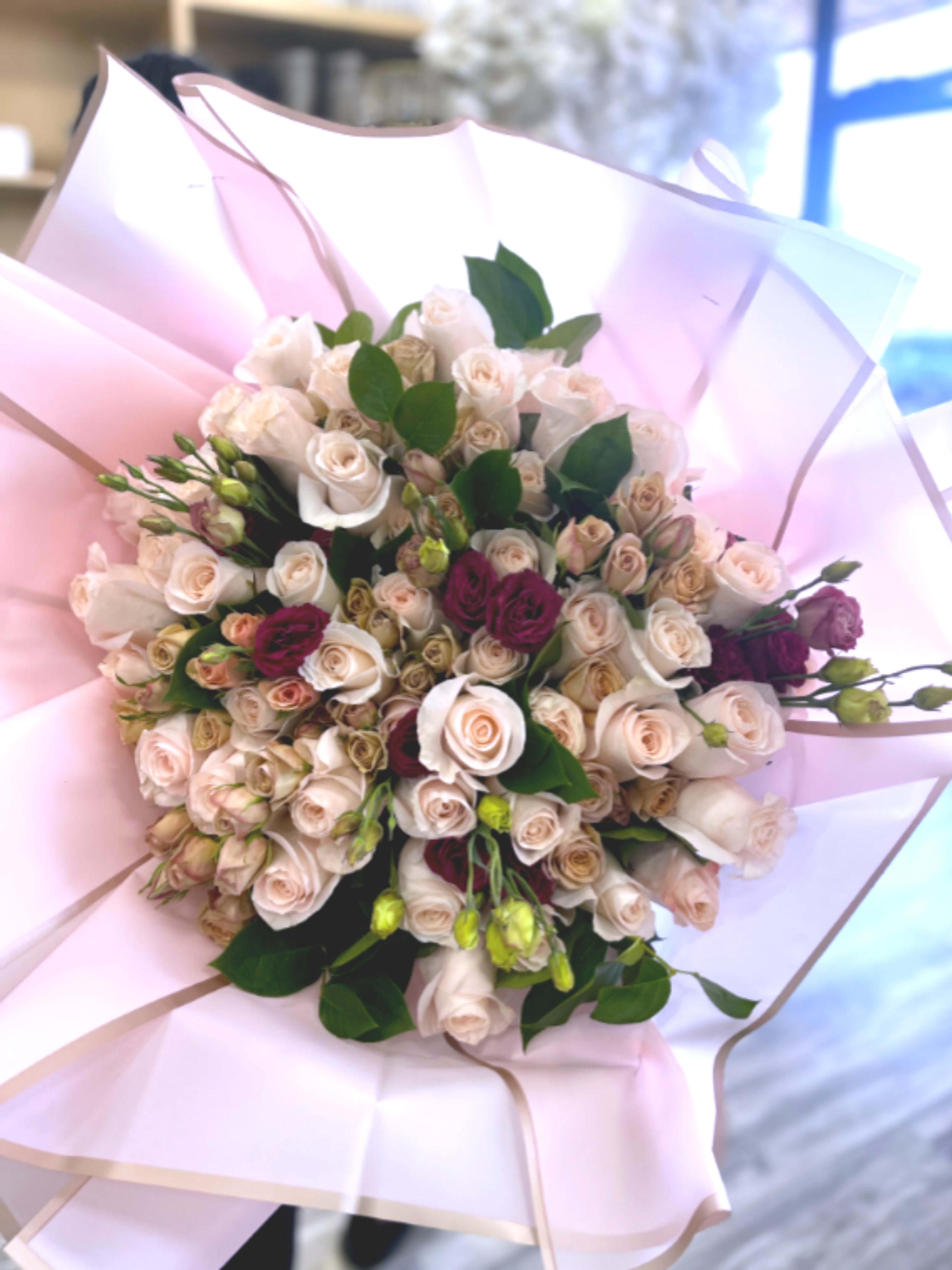 Luxury Cream &amp; Blush Rose Bouquet - This elegant bouquet features premium cream and blush roses accented with rich burgundy spray roses and fresh seasonal greenery. Hand-arranged and wrapped in soft pastel pink paper, it creates a romantic and sophisticated floral display perfect for special occasions, celebrations, or thoughtful gifting.  Designed to impress, this bouquet blends soft neutral tones with deep floral accents for a luxurious and timeless look.