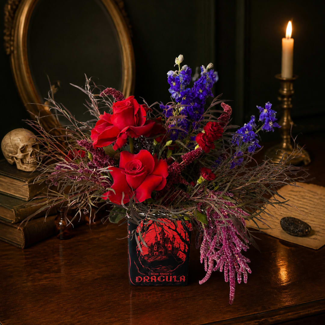 Red roses and purple flowers in a Dracula tin vase with a lit candle nearby.
