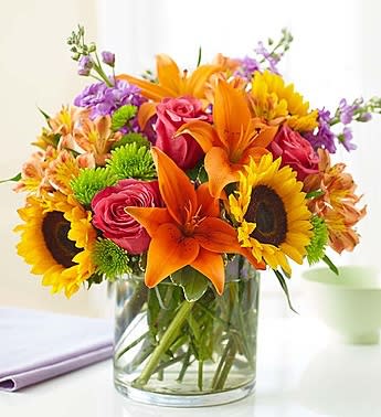 Mixed bouquet of sunflowers, orange lilies, and pink roses in a glass vase