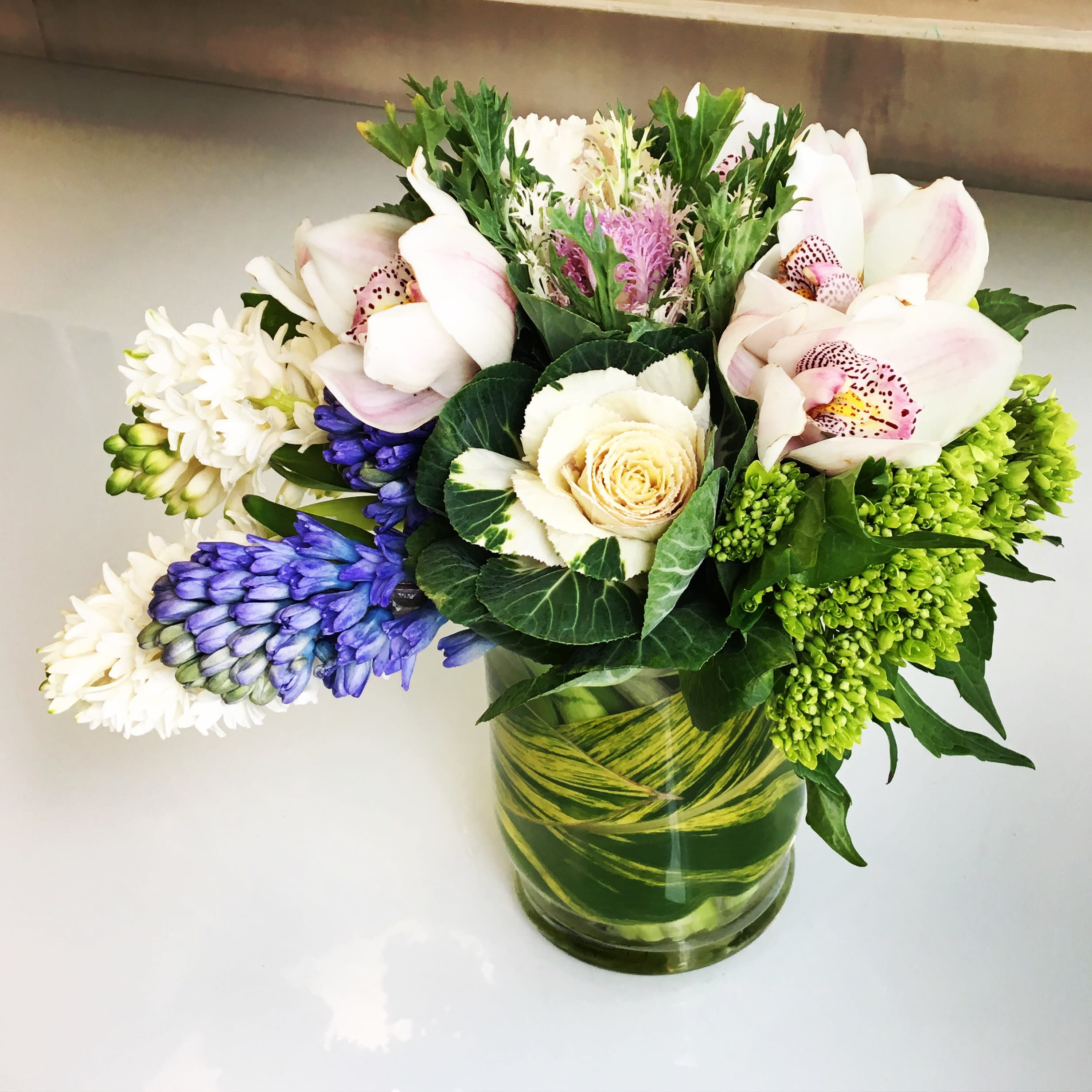 Mixed bouquet with orchids, roses, and blue flowers in a glass vase