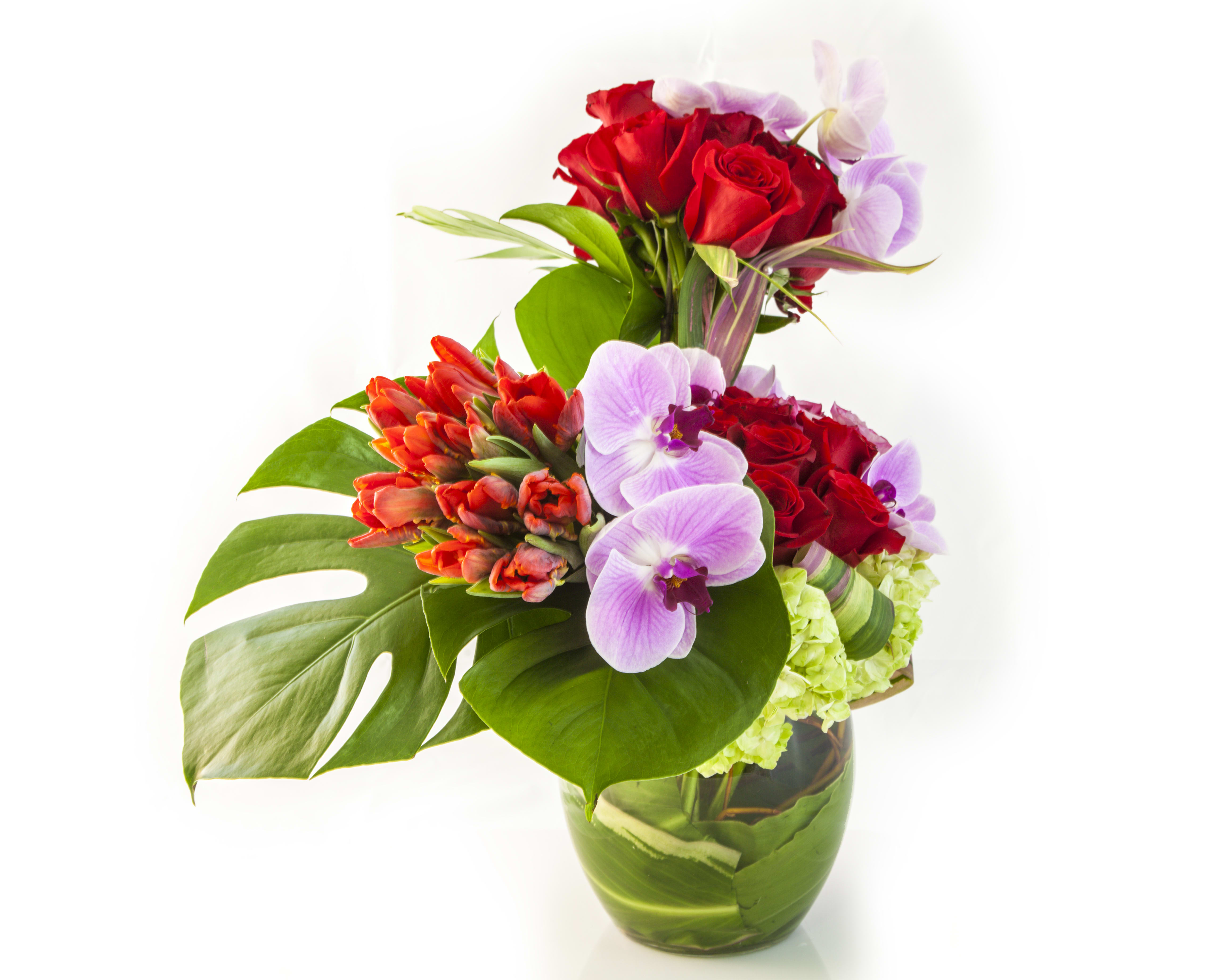 Bouquet of red roses, purple orchids, and orange tulips in a glass vase