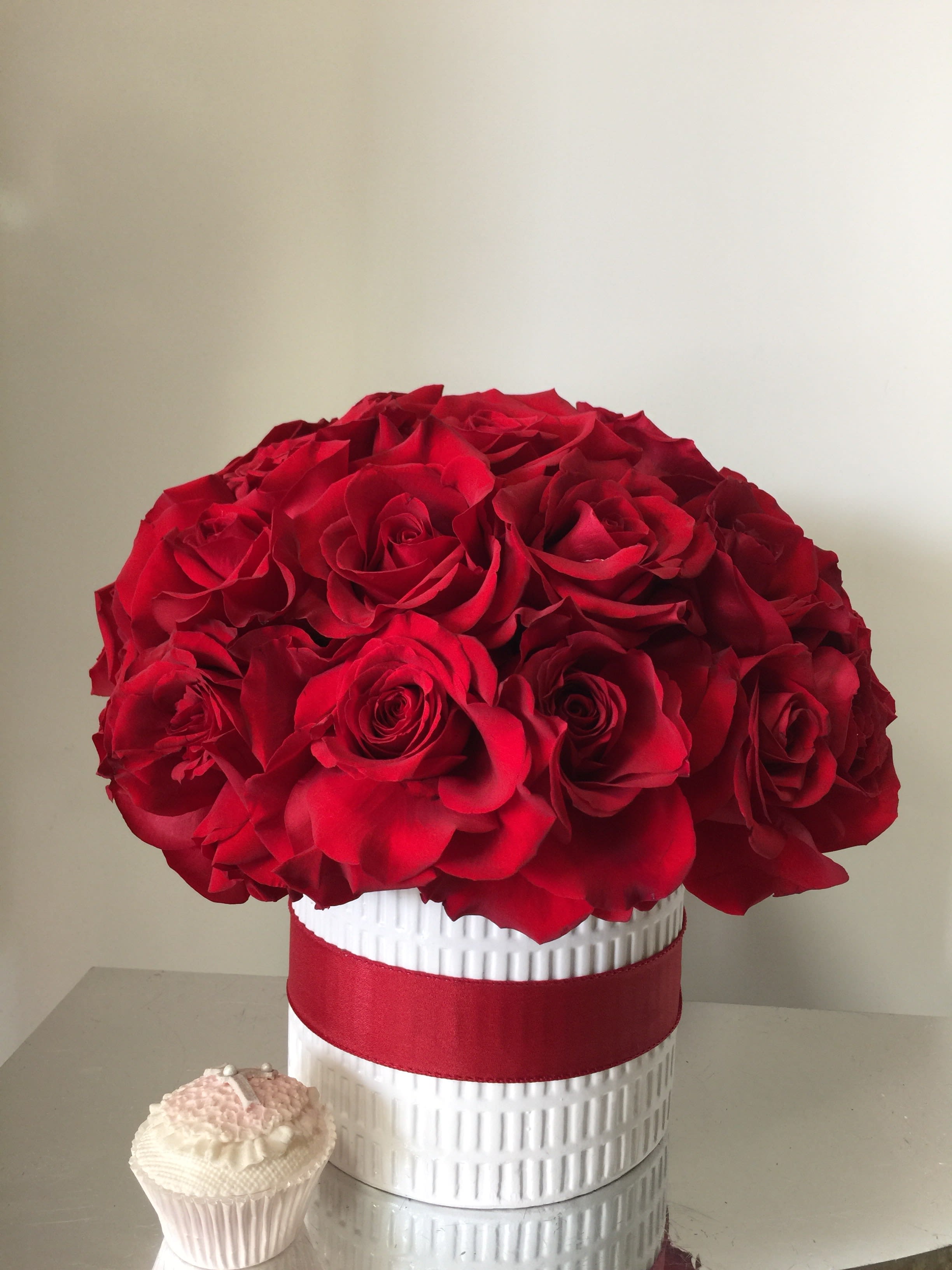 Red rose bouquet in a white textured vase with a red ribbon