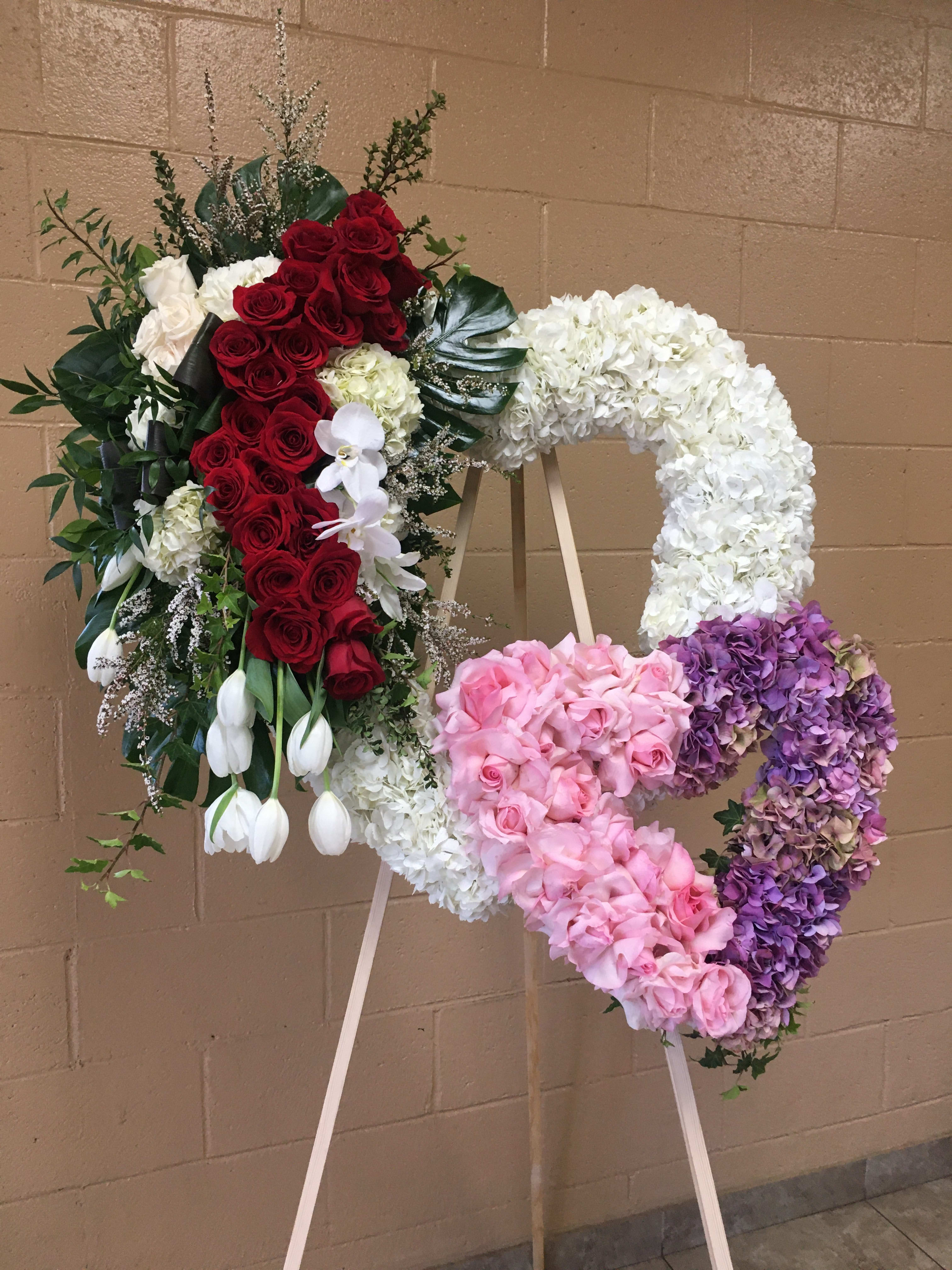 Heart-shaped floral wreath on an easel with red, white, pink, and purple flowers