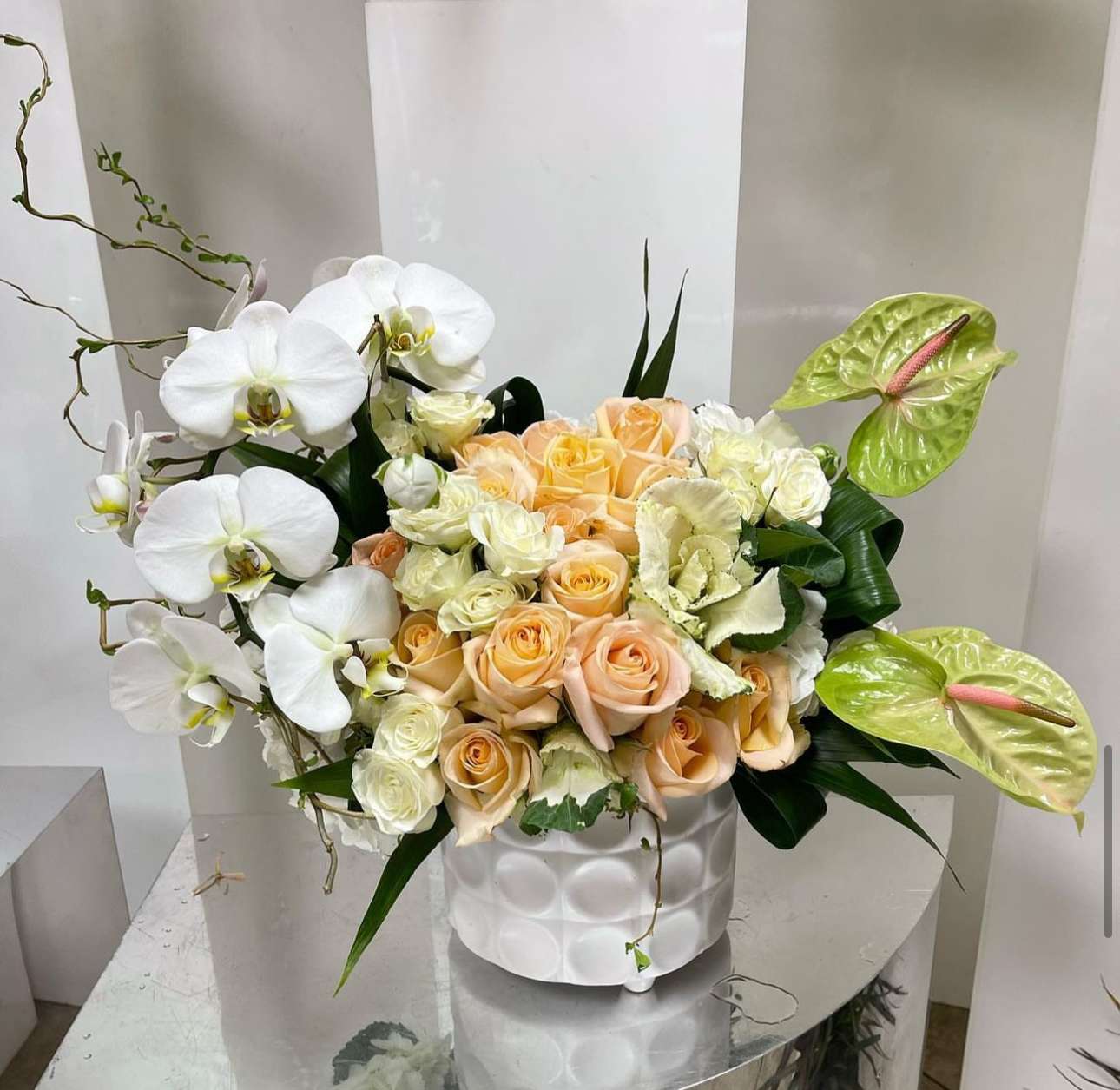 White orchids and peach roses in a white vase with green anthuriums