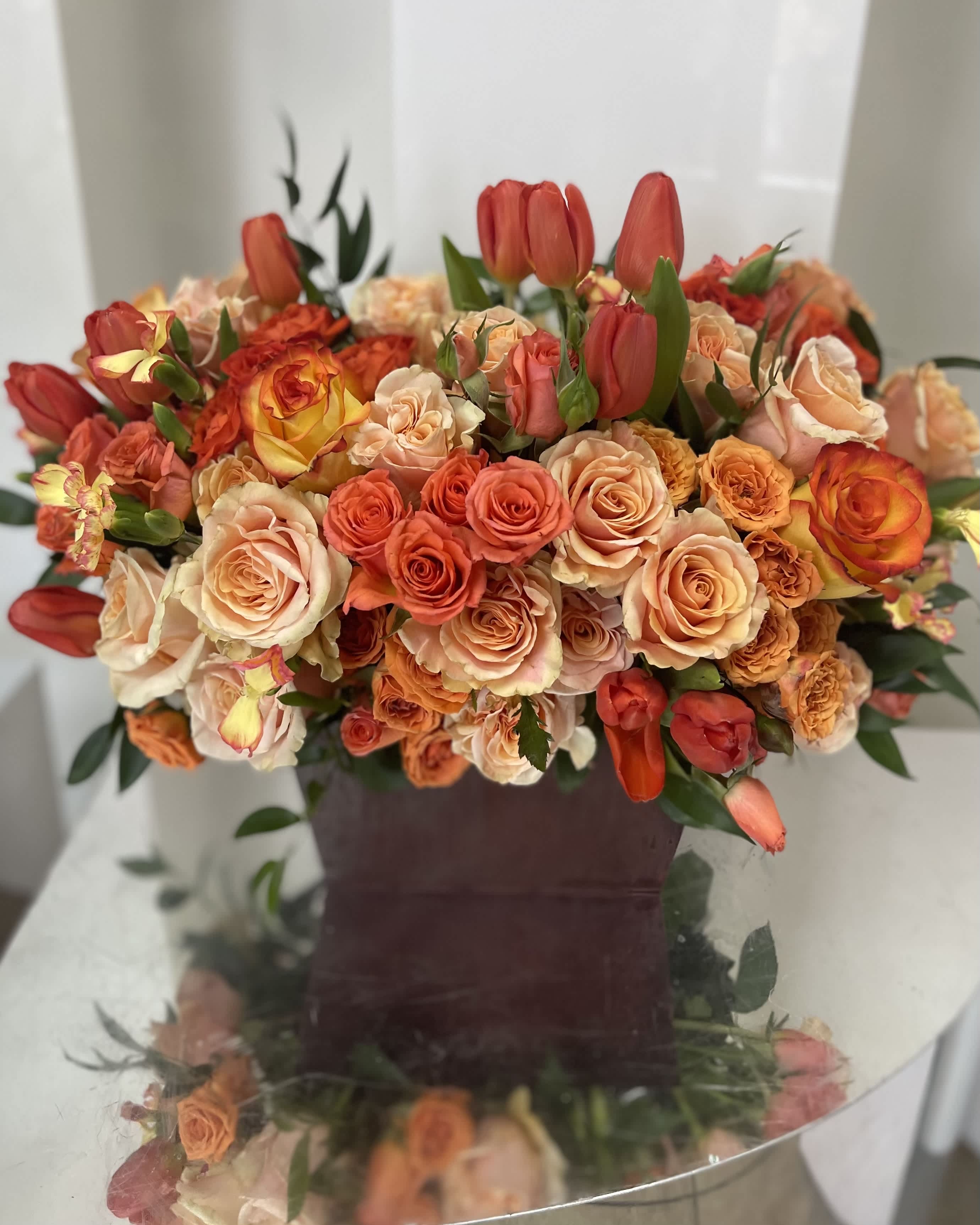 Bouquet of peach and orange roses with red tulips in a dark vase