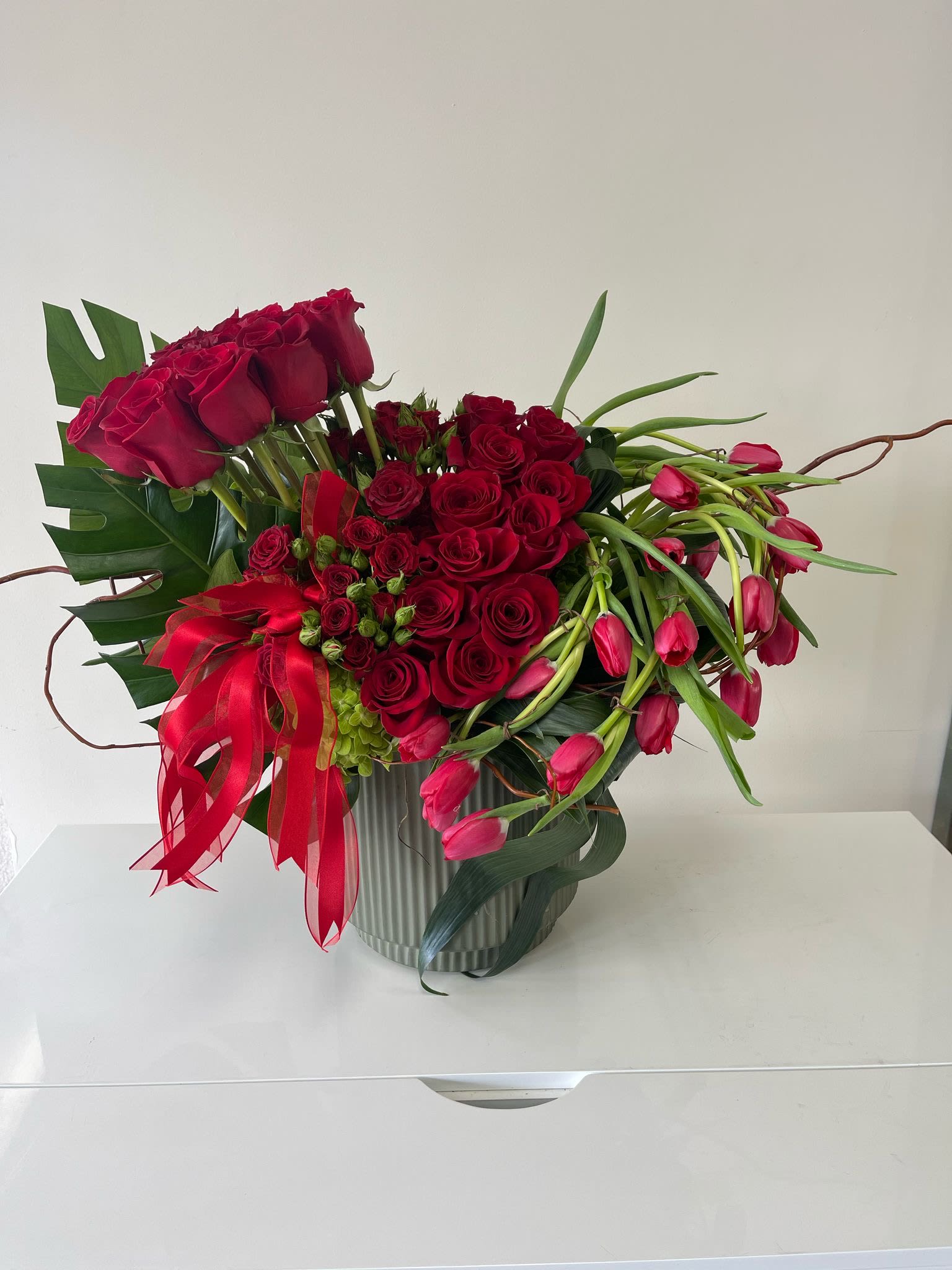 Red roses and pink tulips arranged in a ribbed vase with a red ribbon