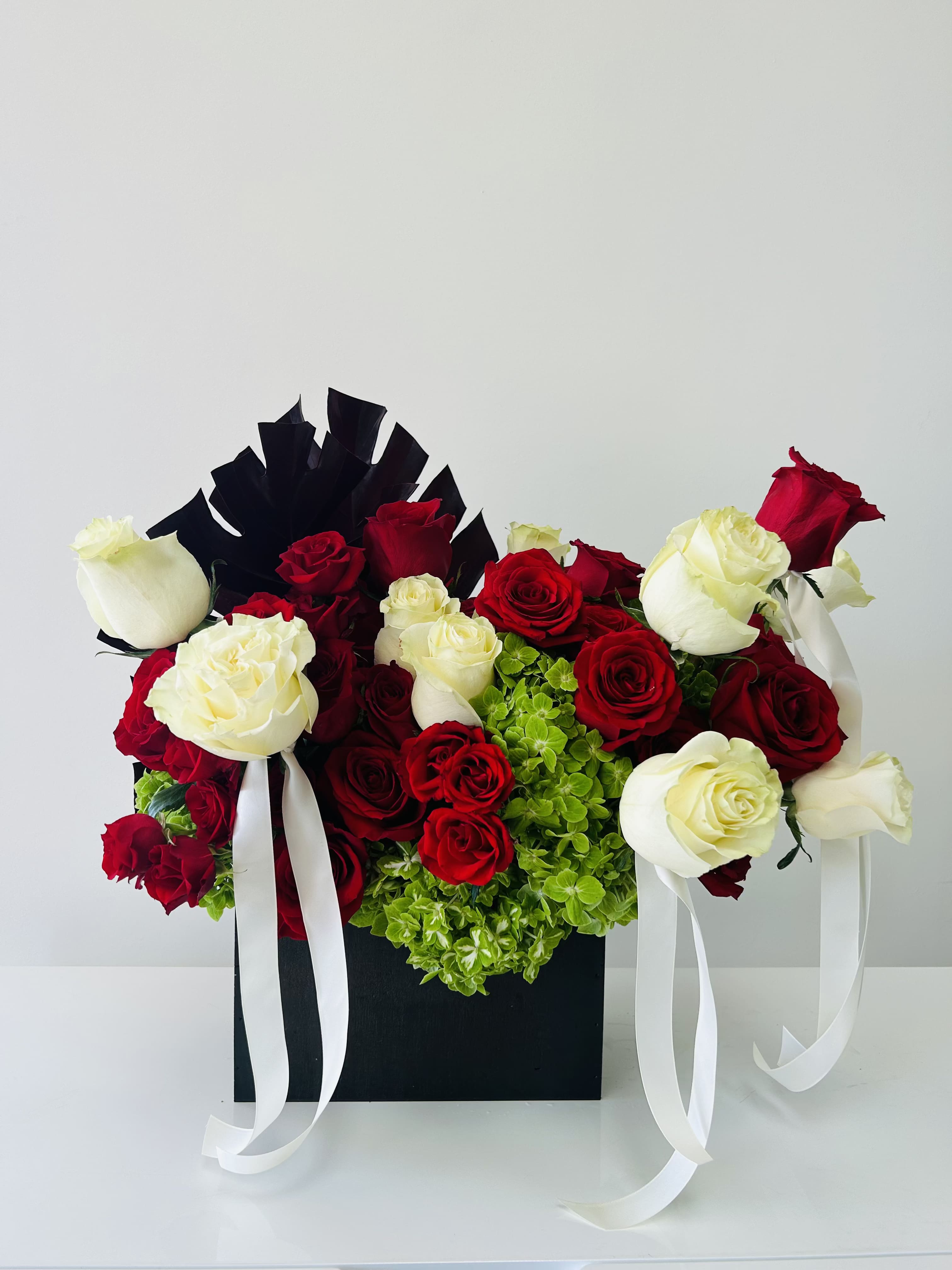 Red and white roses arranged in a black box with white ribbons
