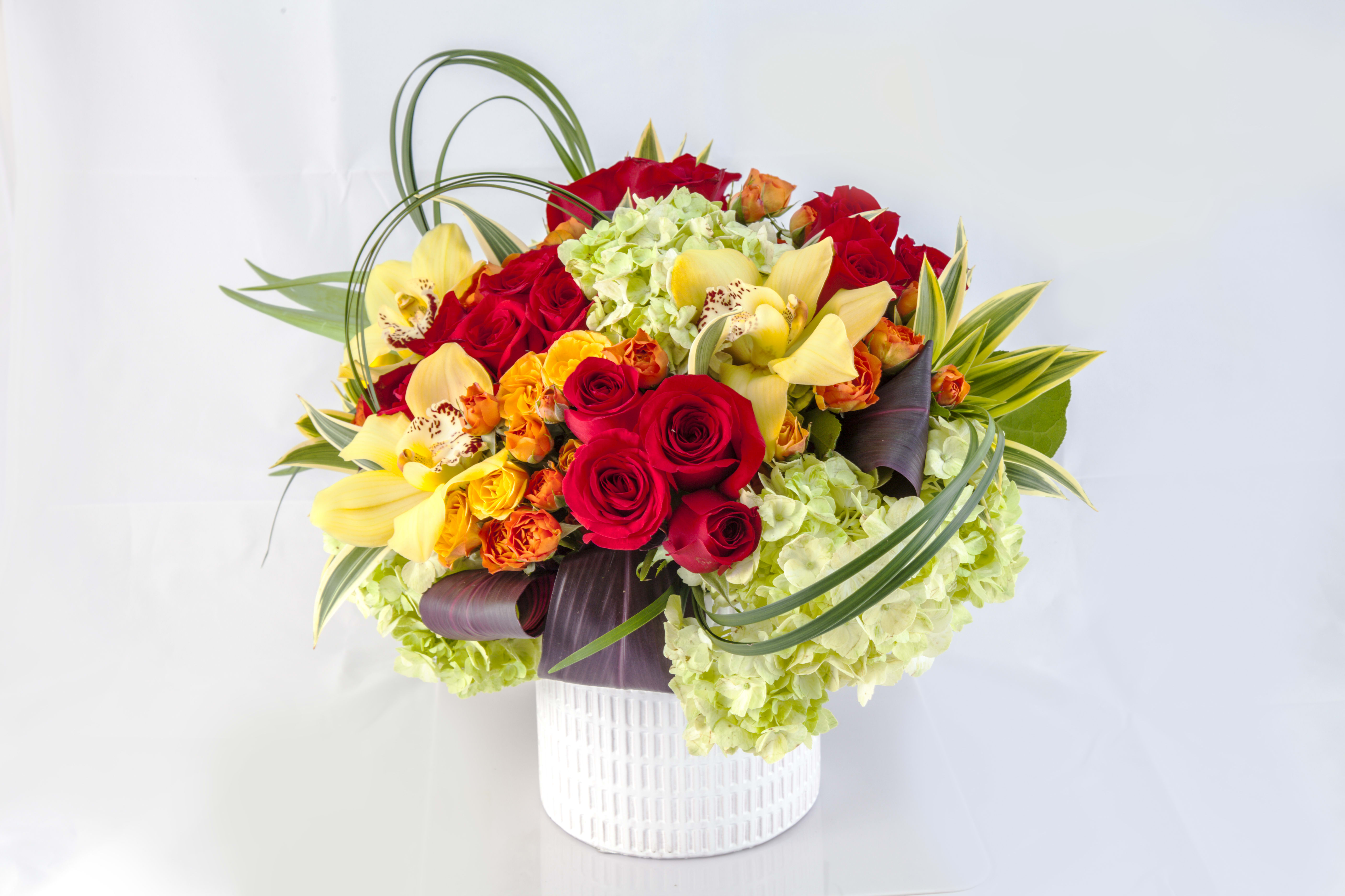 Bouquet of red roses, yellow orchids, and green hydrangeas in a white vase