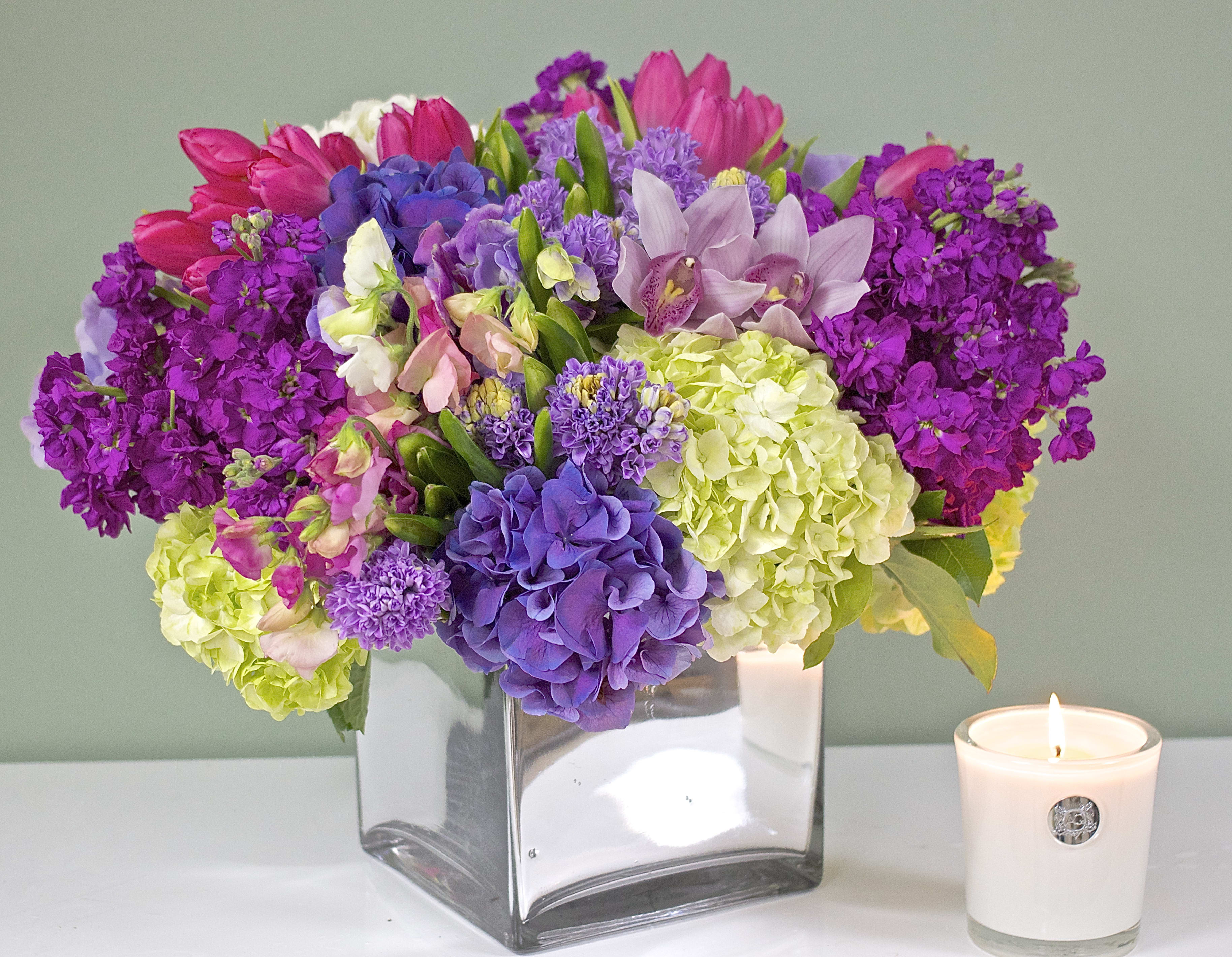 Purple Hydrangea and Tulip Mix - Purple Hydrangea and Tulip  Mix  Approx. 15" Wide X 15" High. Candle not included. 20 Dutch Tulips, 10 Cymbidium Orchid Blooms, sweet peas, 10 Hyacinths and 40 stems of season Blooms in a Chrom Glass Vase.