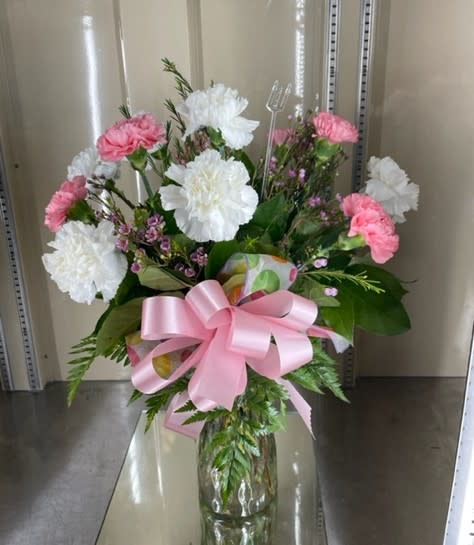 Pink and white carnations in a glass vase with a pink ribbon