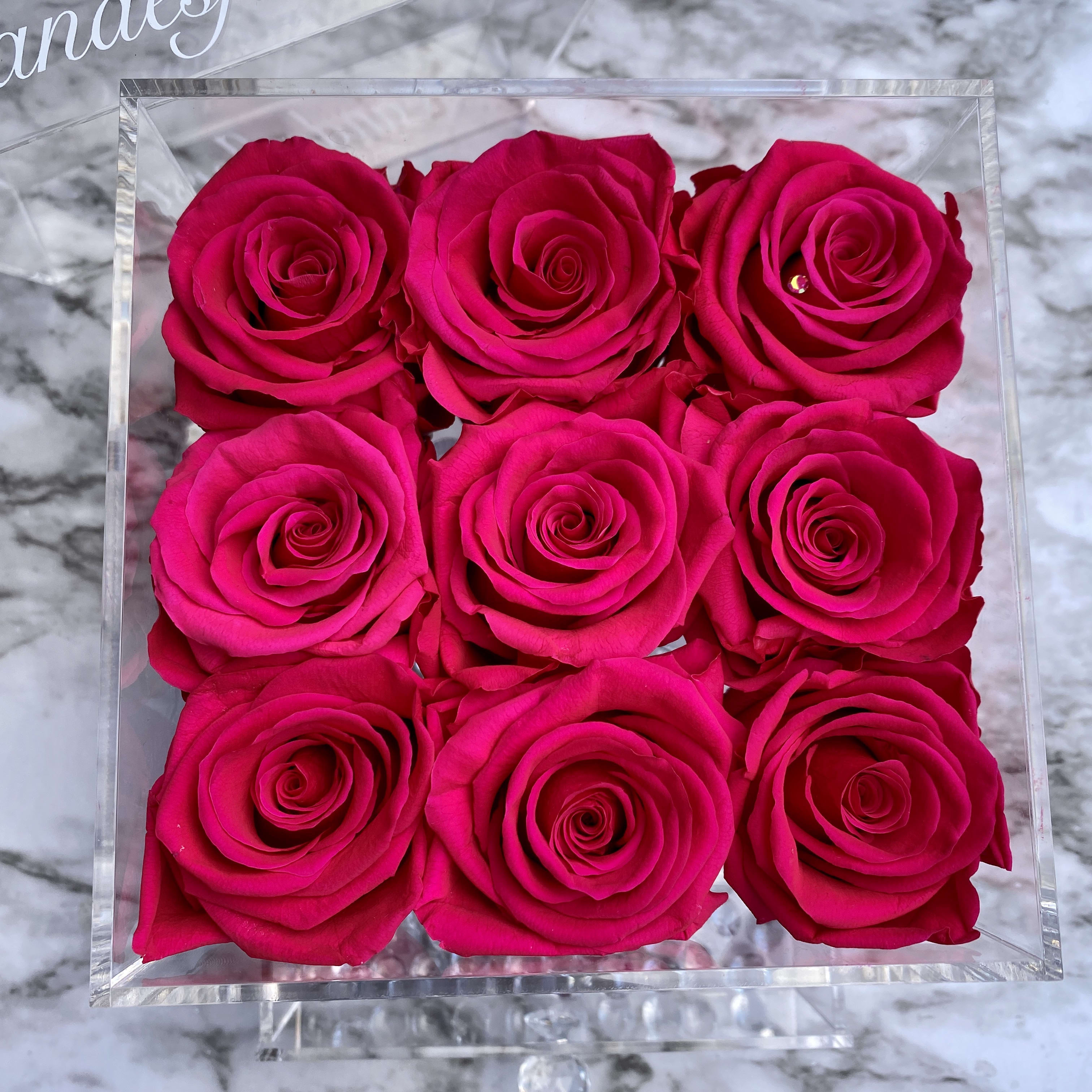 Nine hot pink roses arranged in a clear square box