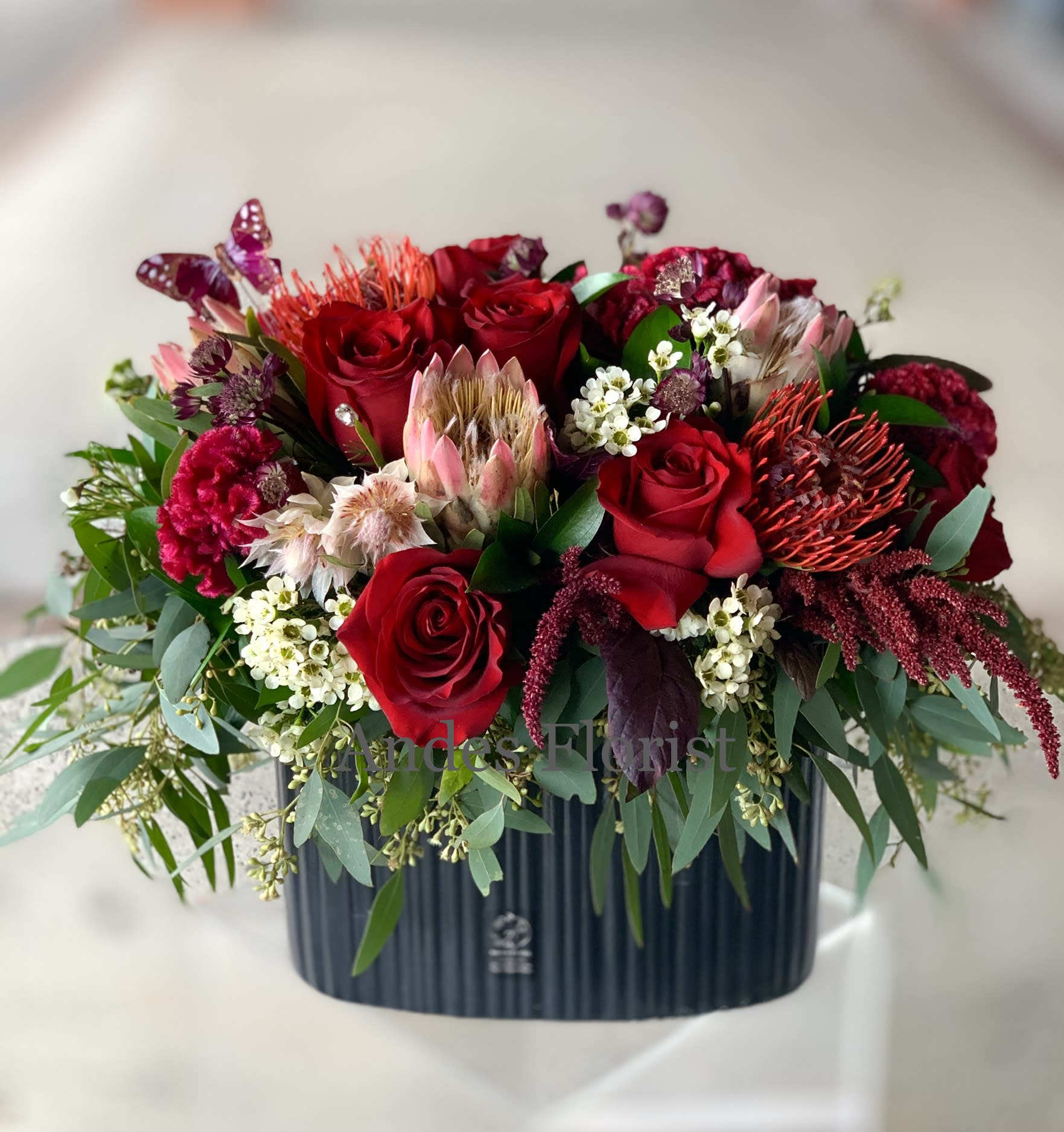 Red roses and mixed blooms arranged in a dark rectangular vase