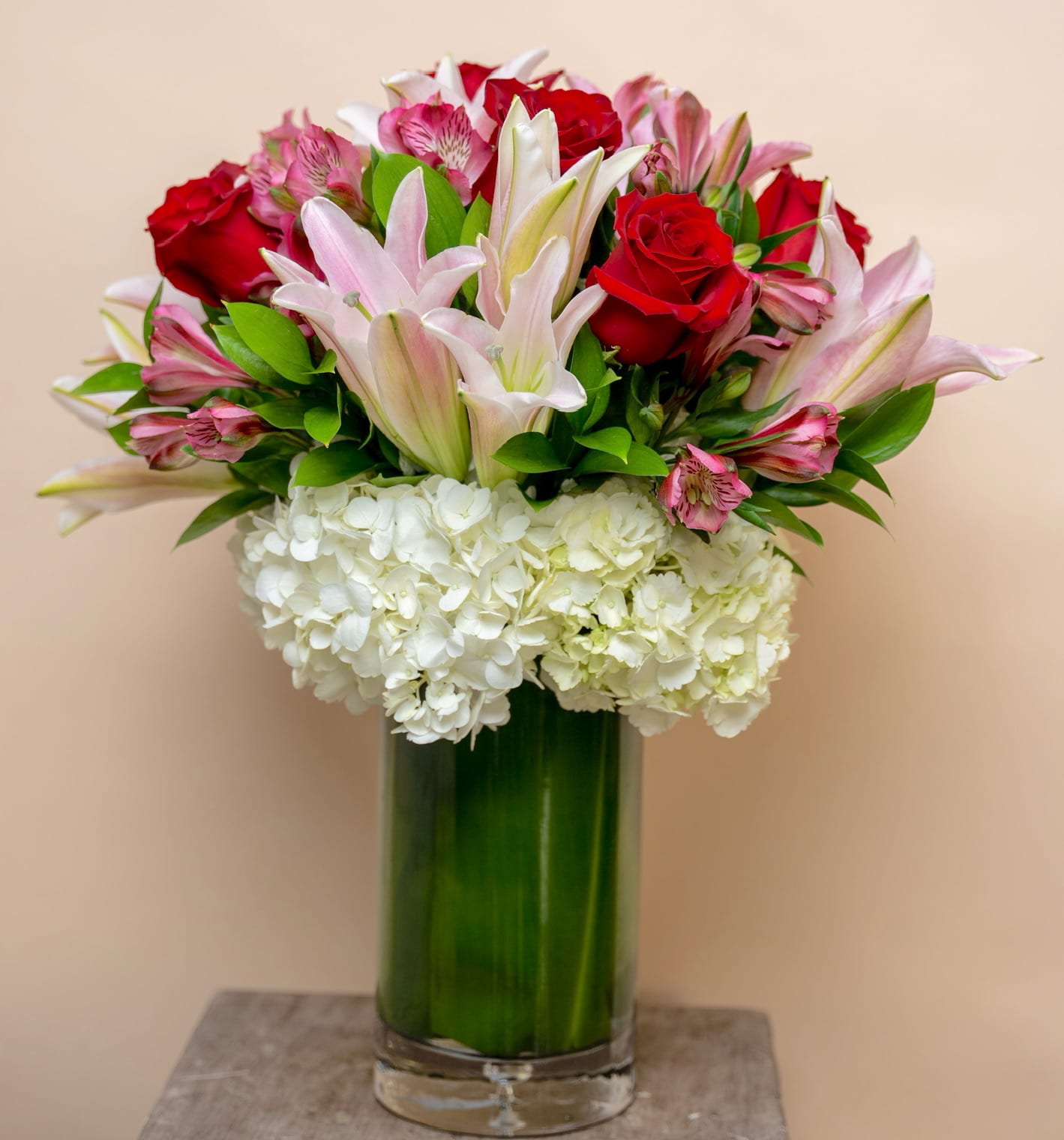Bouquet of red roses, pink lilies, and white hydrangeas in a glass vase