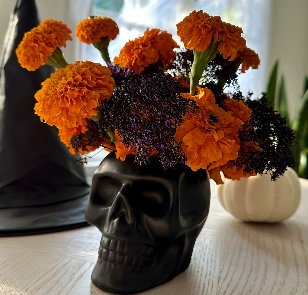Orange marigolds arranged in a black skull vase with dark filler flowers