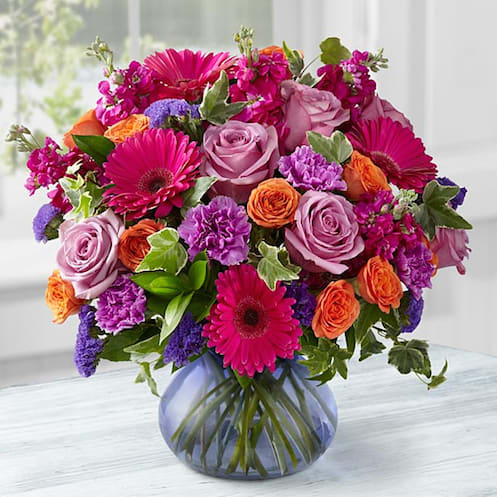 The FTD® Life in Bloom Bouquet by Better Homes and Gardens® - VASE INCLUDED - Picked fresh from the farm and bursting with a bright array of colors, the FTD® Life in Bloom Bouquet by Better Homes and Gardens® is a true marvel. Hand gathered in select floral farms and showcasing the brilliant vibrant colors of fuchsia, lavender, orange and purple, this fresh flower arrangement has been picked fresh for you to help celebrate a birthday, send your get well wishes, or to express your heartfelt thanks and gratitude. This bouquet includes the following: lavender roses, fuchsia stock, orange spray roses, lavender carnations, fuchsia mini gerbera daisies, purple statice, and an assortment of lush greens with a purple glass vase. GOOD bouquet includes 15 stems with vase &amp; approximately 14"H x 13"W. BETTER bouquet includes 19 stems with vase &amp; approximately 14"H x 14"W. BEST bouquet includes 24 stems with vase &amp; approximately 15"H x 15"W. Your purchase includes a complimentary personalized gift message.