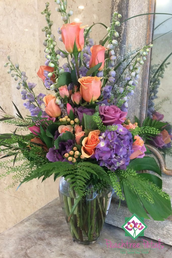 Tall bouquet of peach roses and purple hydrangeas in a glass vase