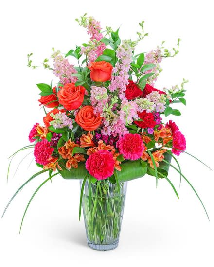 Mixed bouquet of roses, carnations, and pink filler flowers in a glass vase