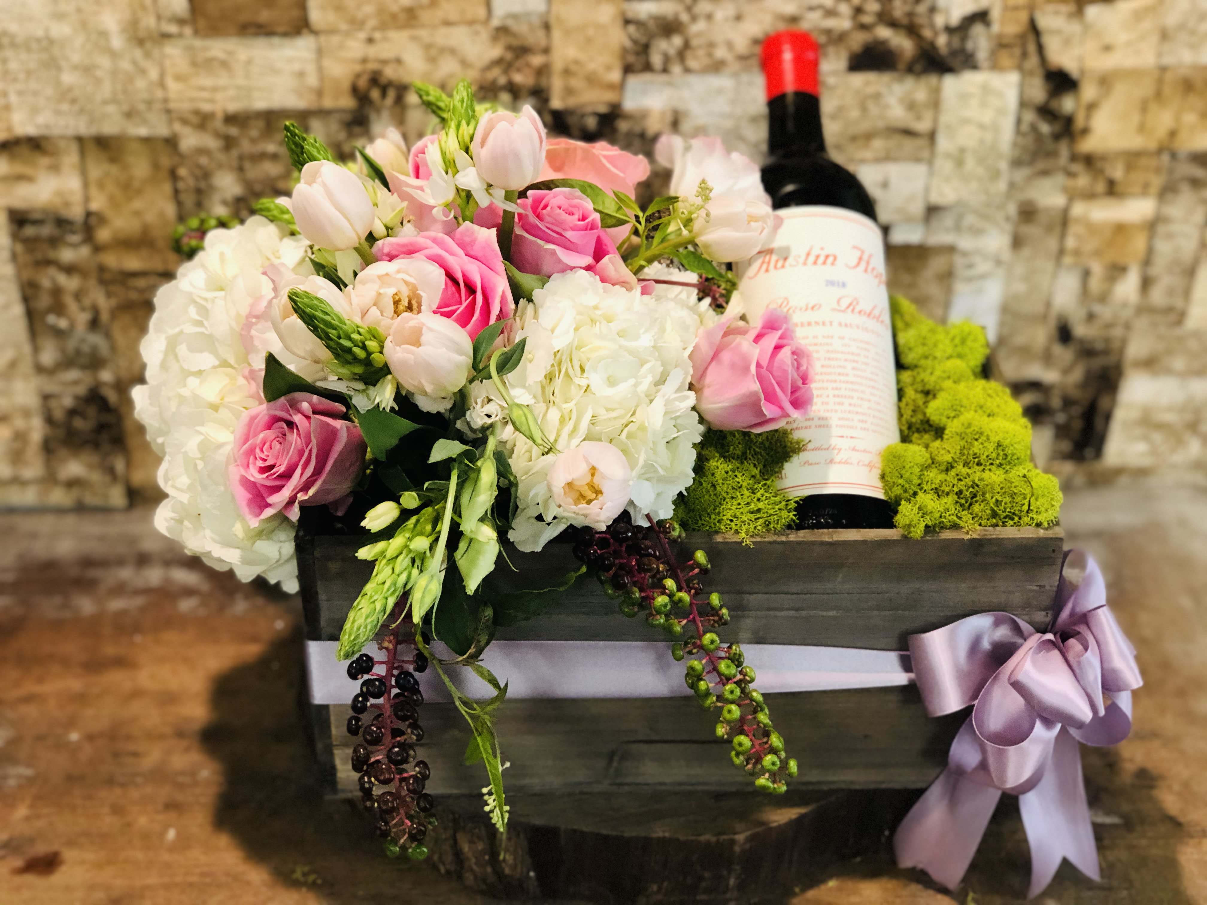 Pink and white floral arrangement in a wooden box with a wine bottle