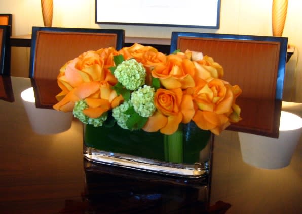 Orange roses arranged in a square glass vase with green blooms