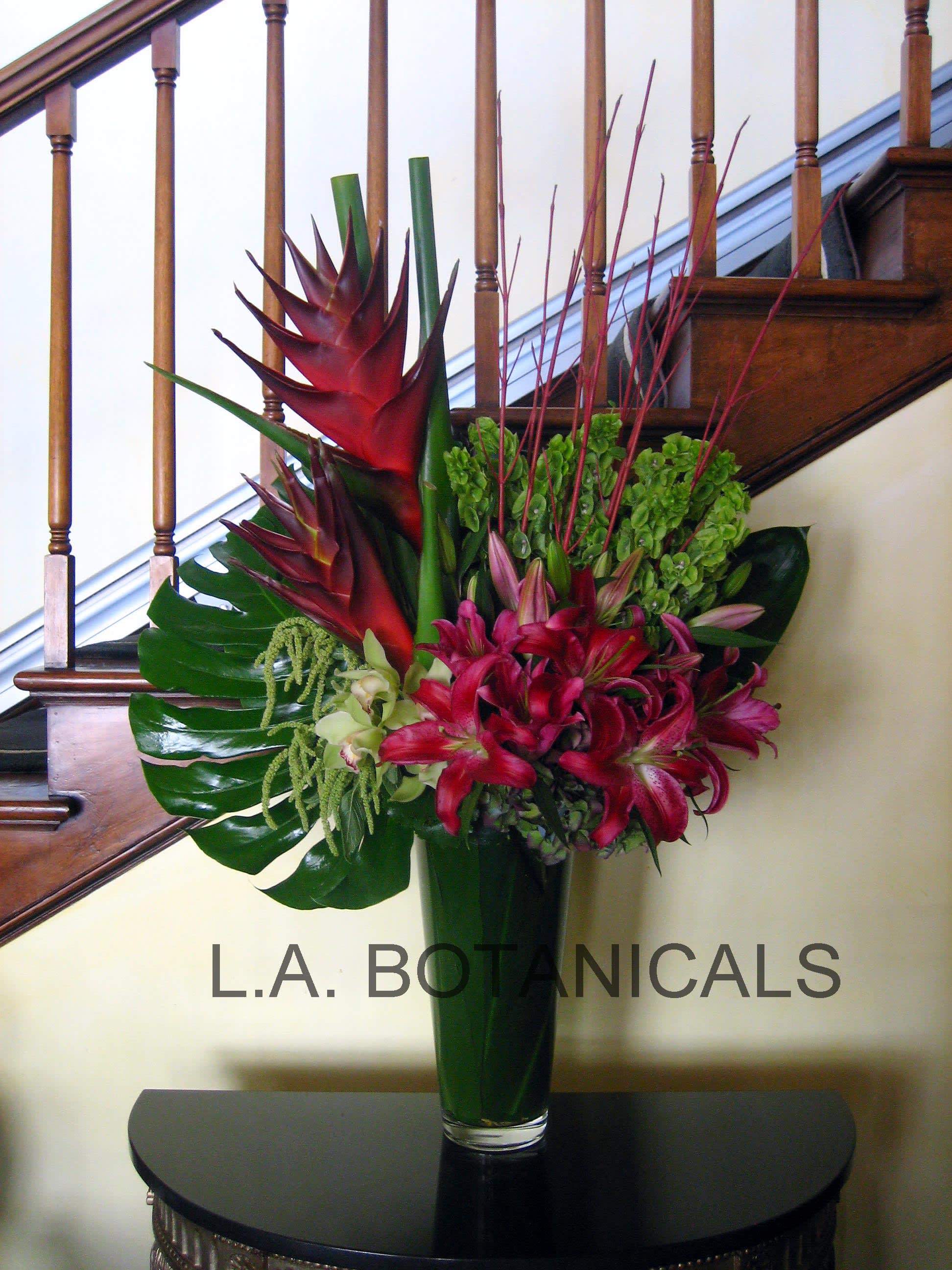 Tropical flower arrangement in a tall glass vase with red lilies and green foliage