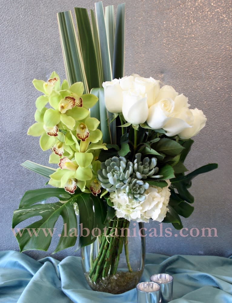 White roses and green orchids in a glass vase with tropical leaves