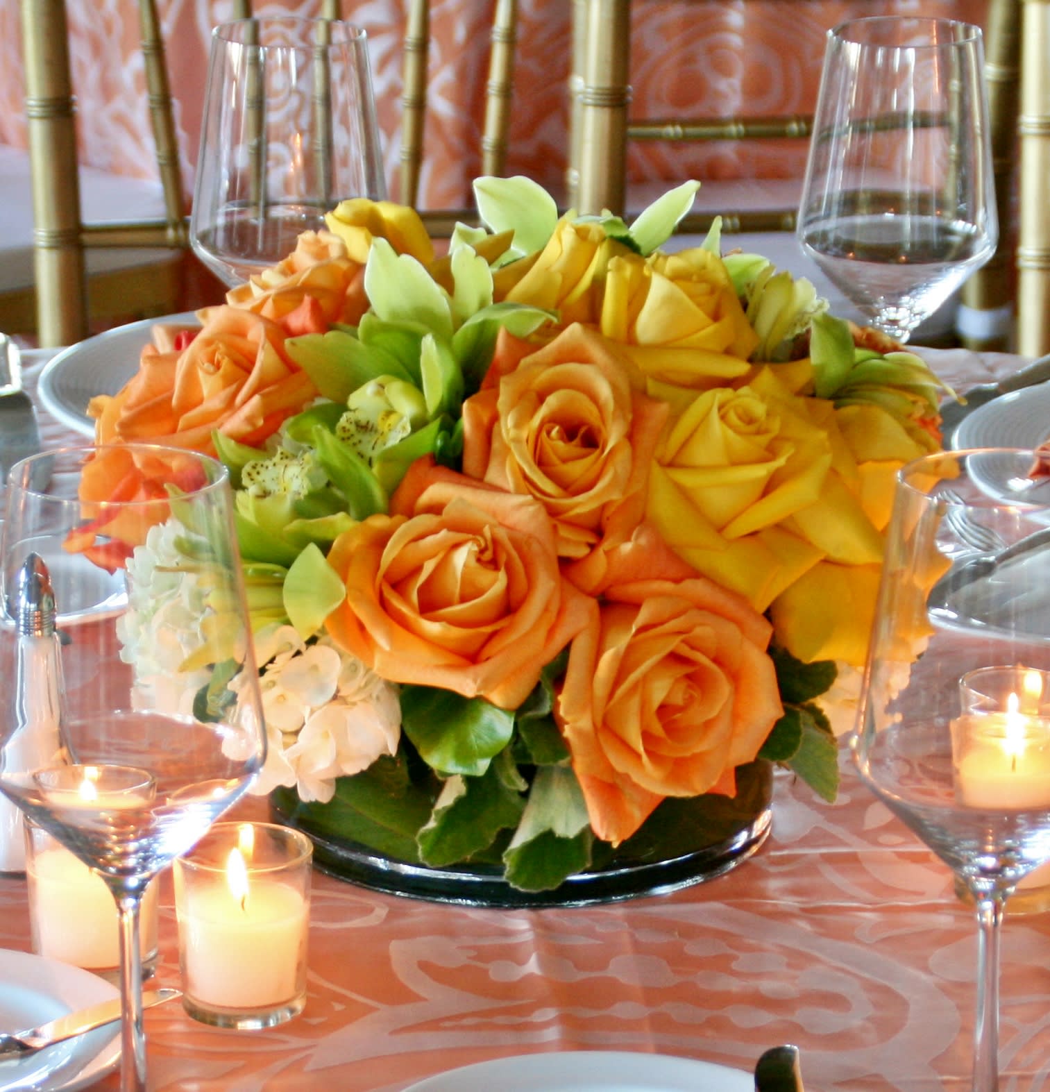 Orange and yellow rose centerpiece on a table with candles and wine glasses