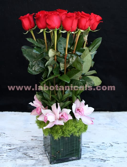 Tall arrangement of red roses and pink orchids in a square glass vase