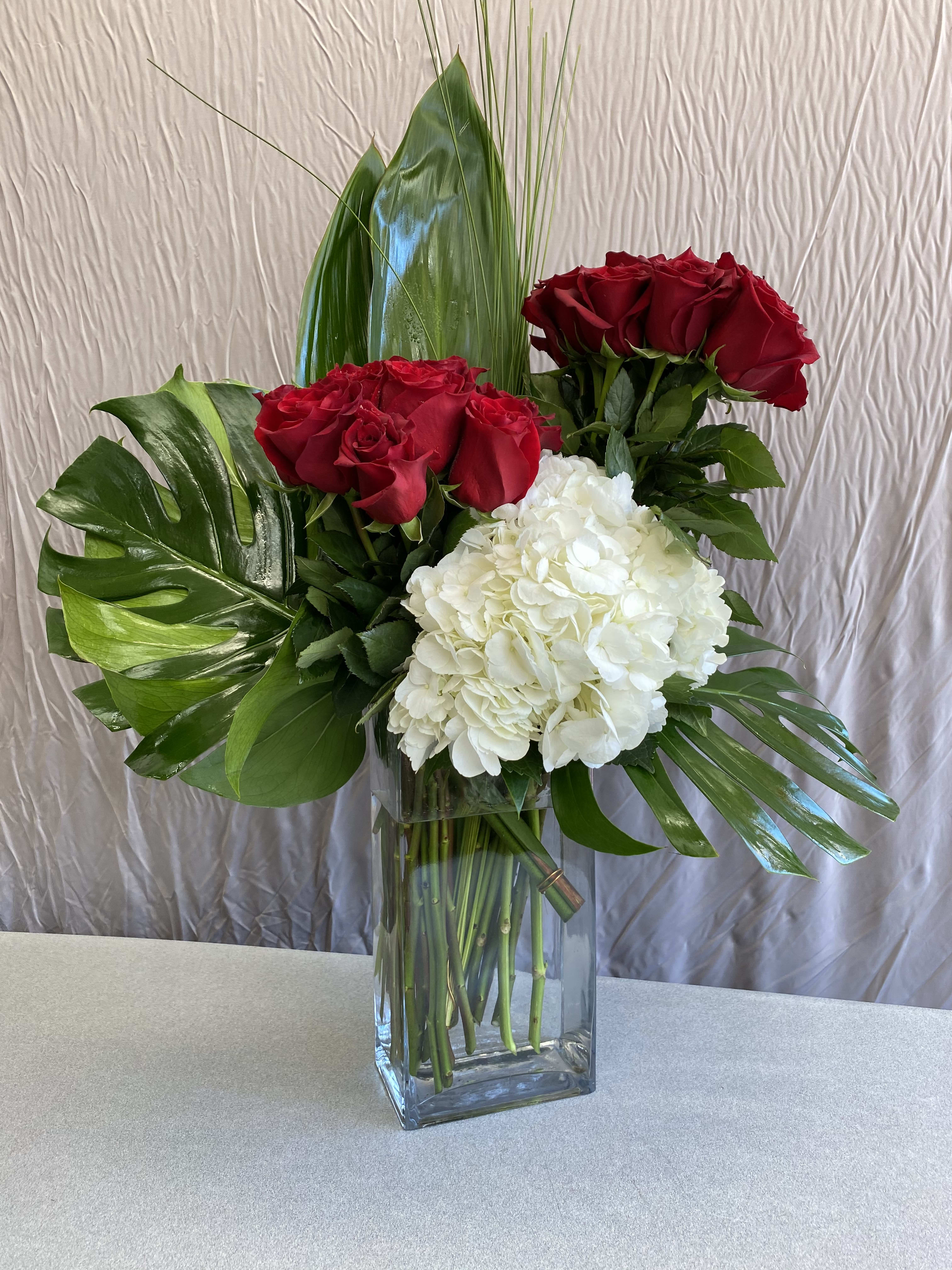 Red roses and white hydrangea in a clear glass vase with tropical leaves