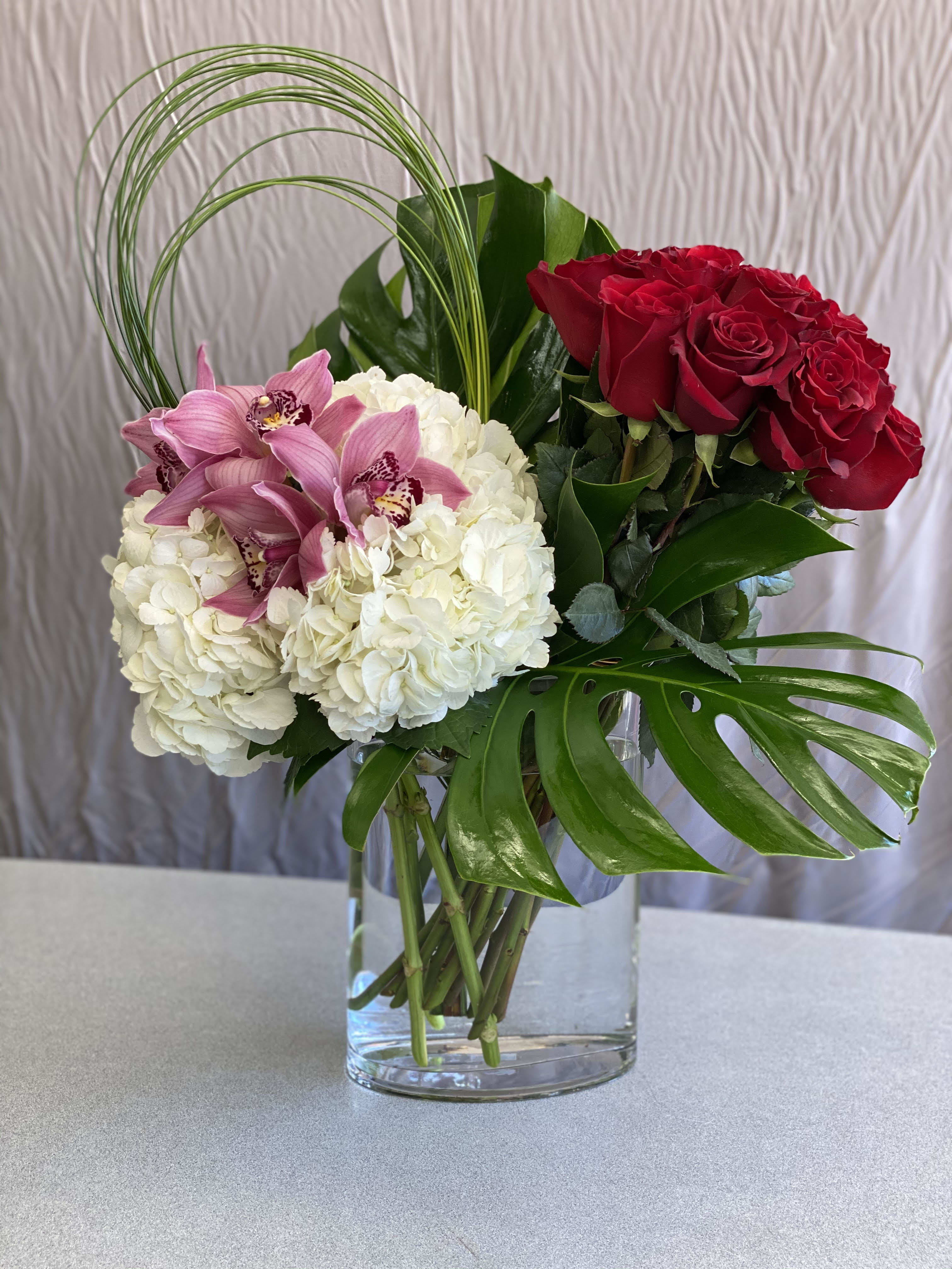 Bouquet of red roses, white hydrangeas, and pink orchids in a glass vase
