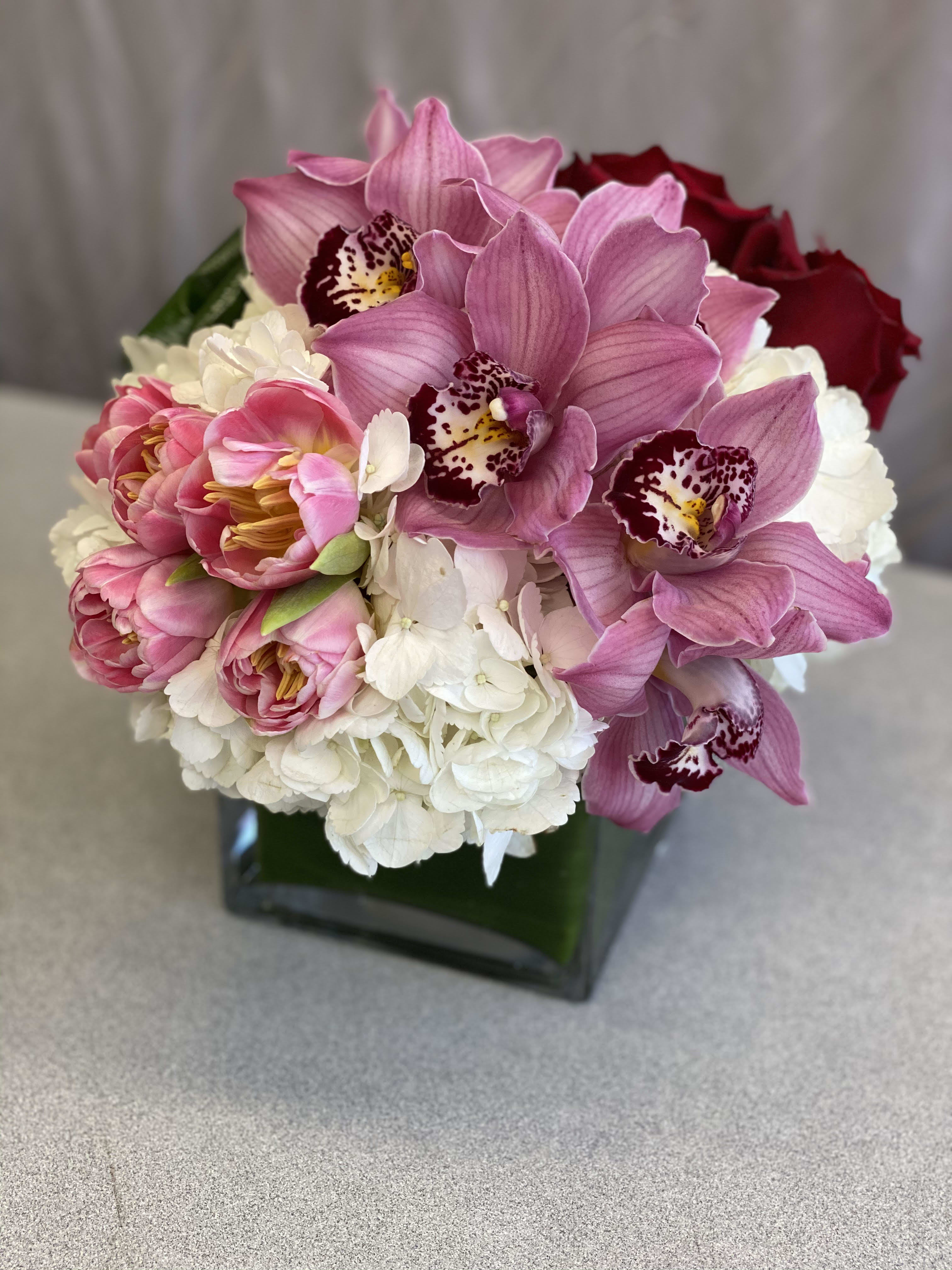 Pink orchids and roses arranged in a square glass vase