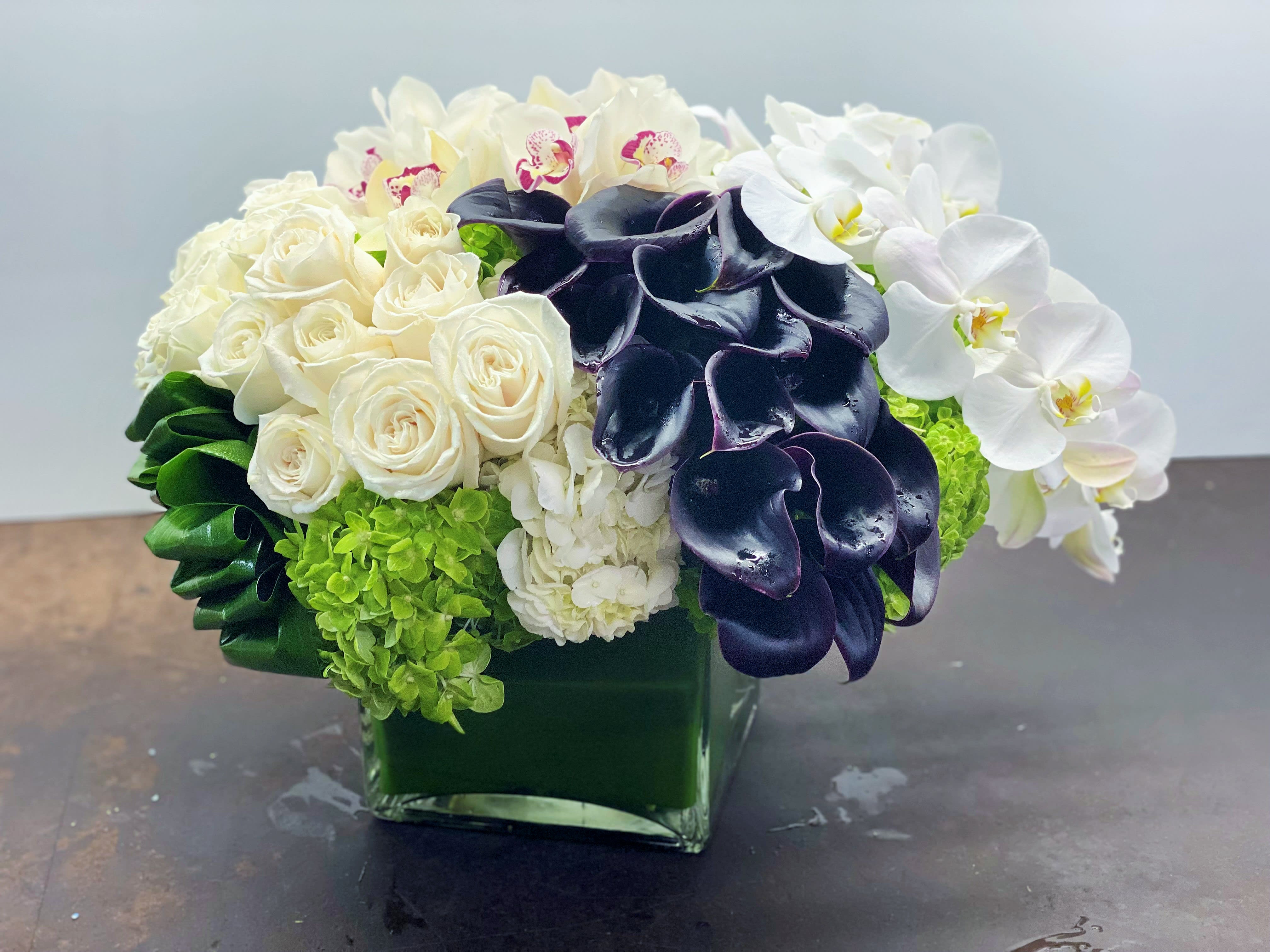 White roses, orchids, and dark calla lilies in a green glass vase