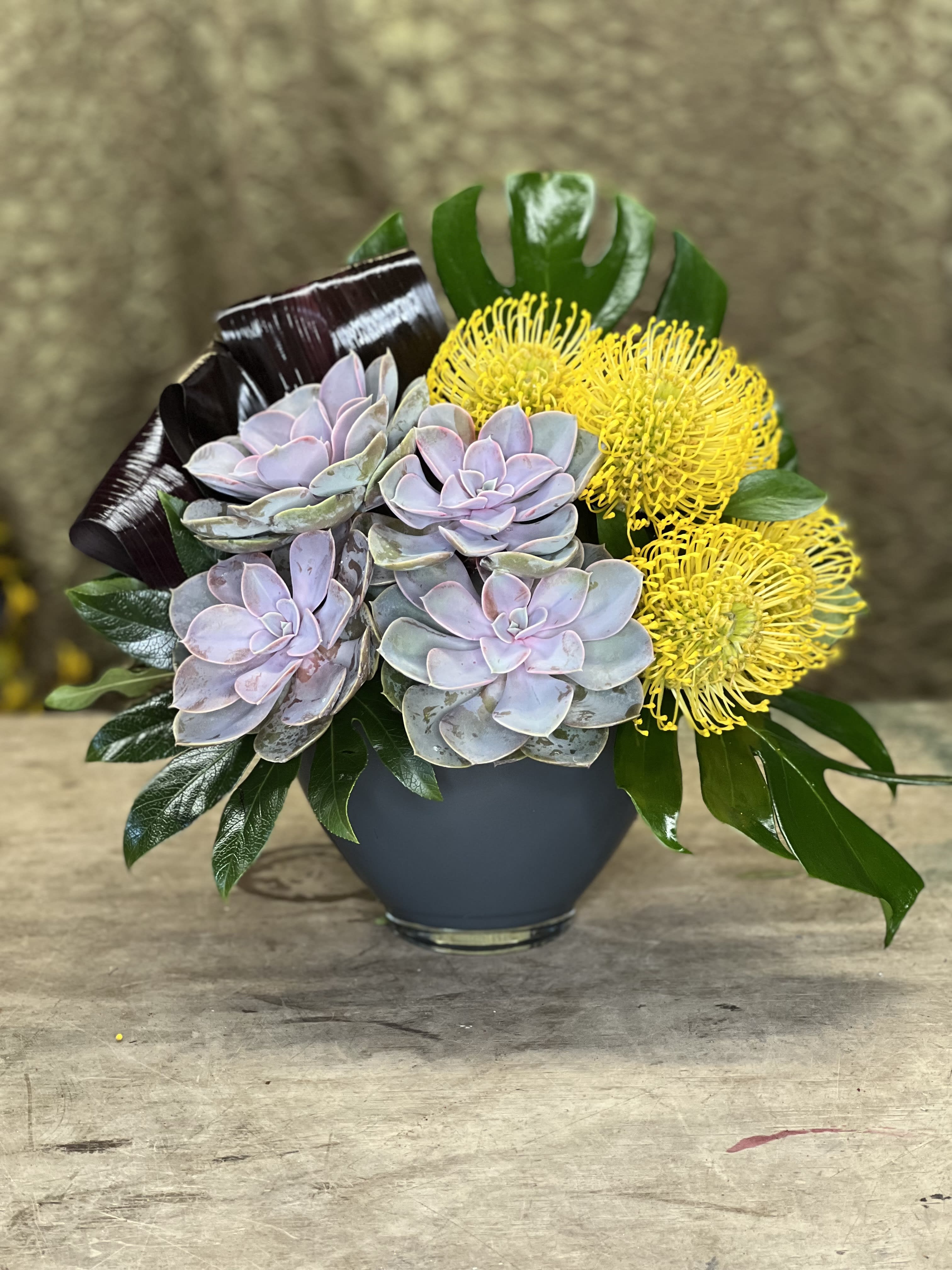 Succulent arrangement with yellow pincushion blooms in a dark vase