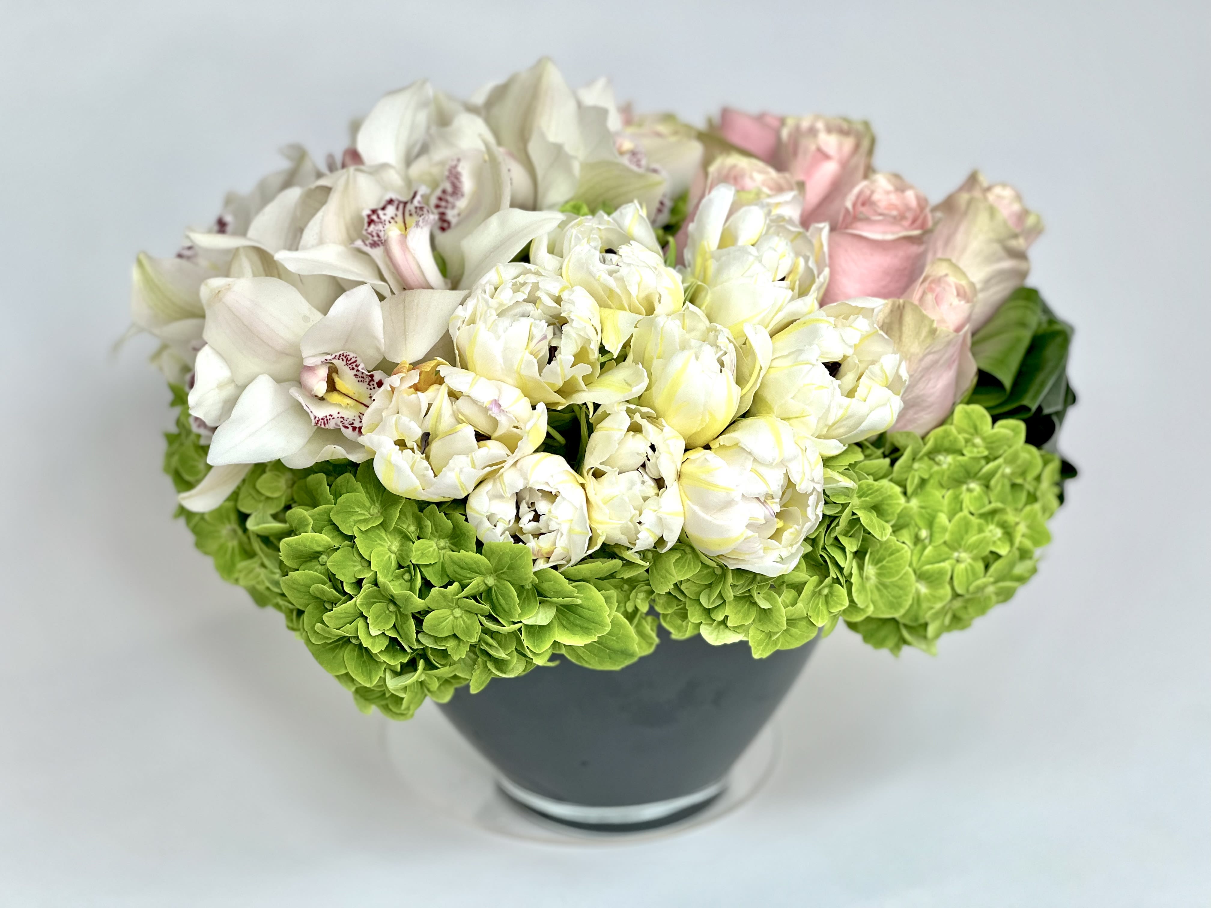 White orchids and pale pink roses in a dark vase with bright green hydrangeas