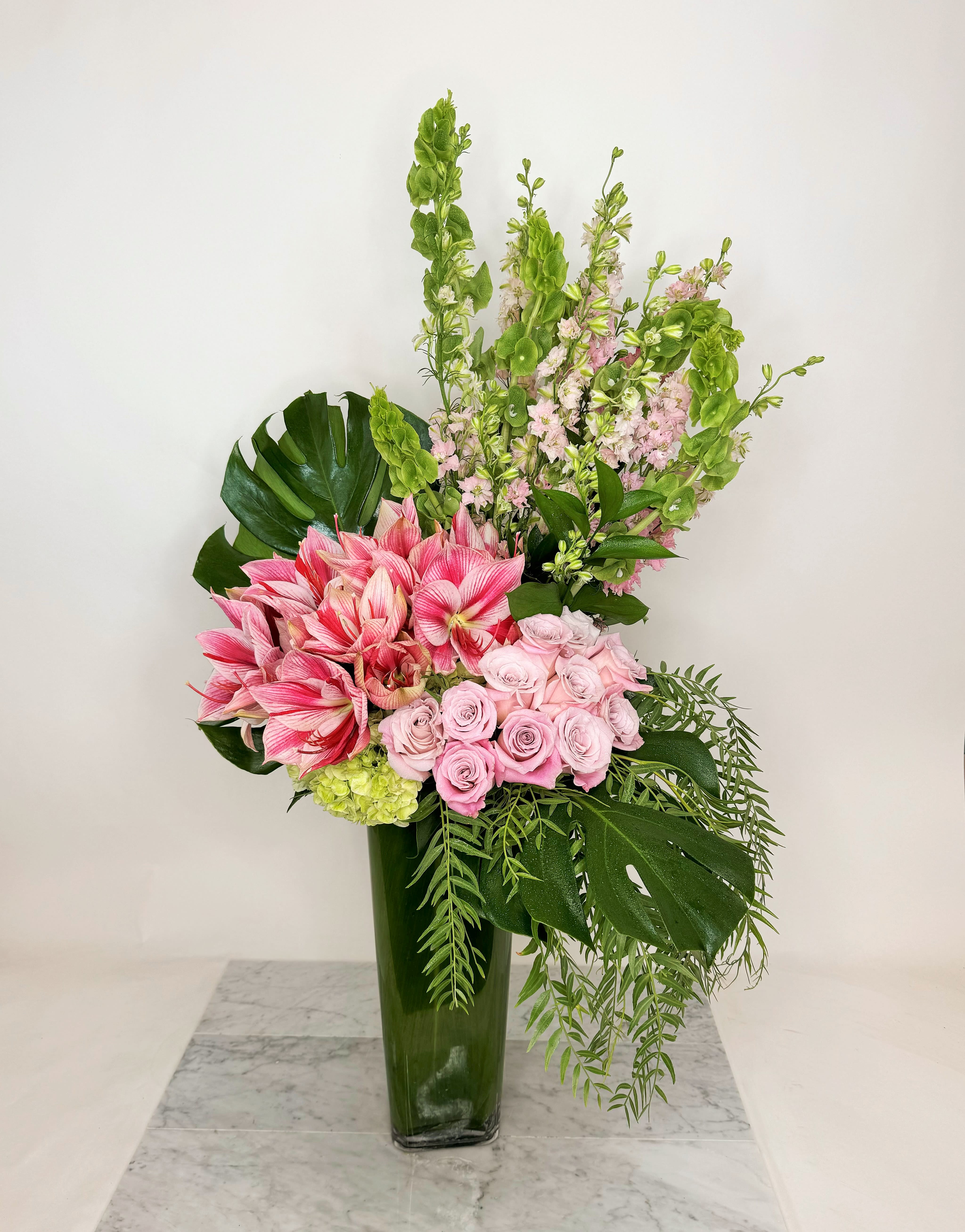 Pink roses and amaryllis in a tall green vase with tropical foliage