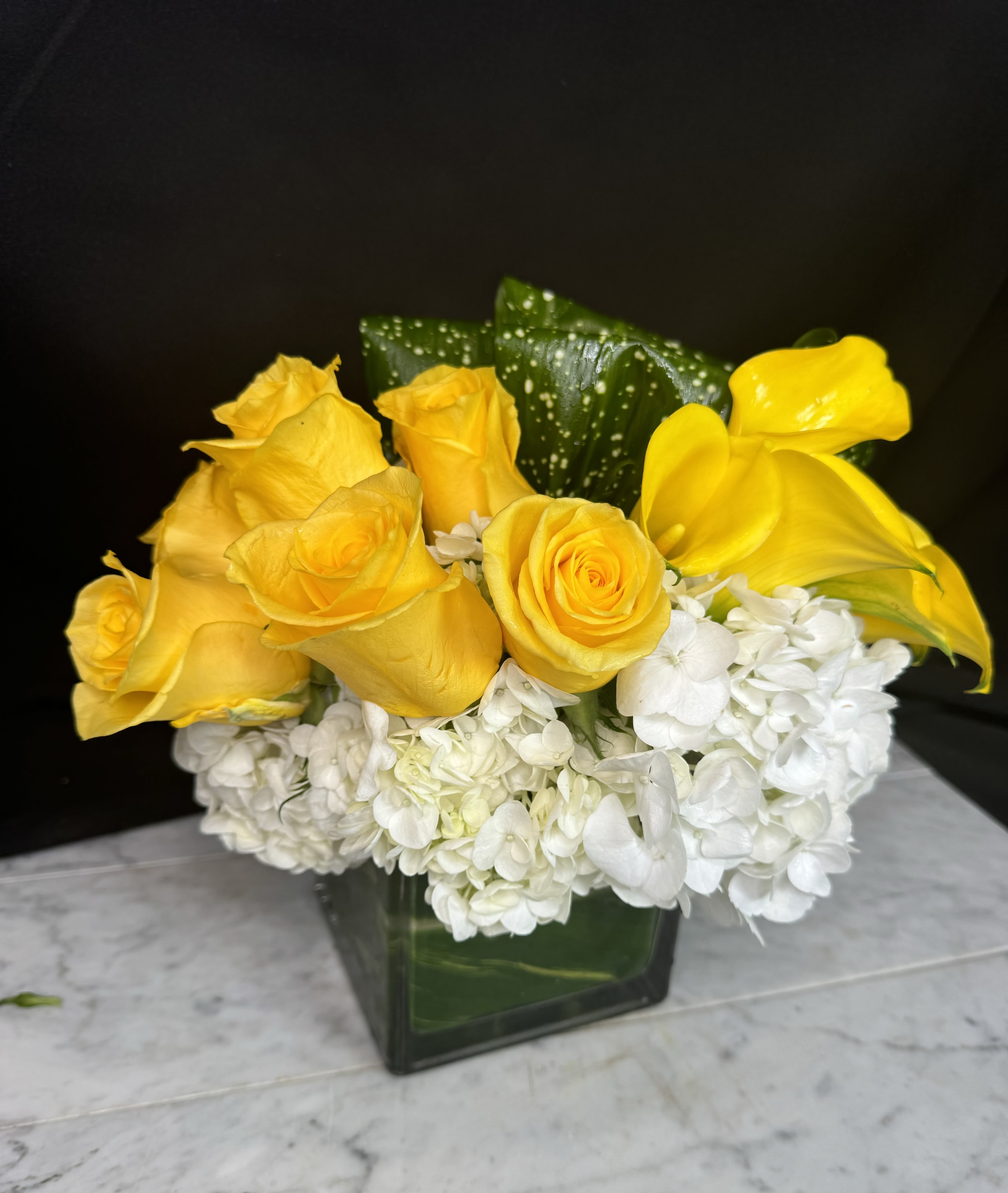 Yellow roses and white hydrangeas in a square glass vase