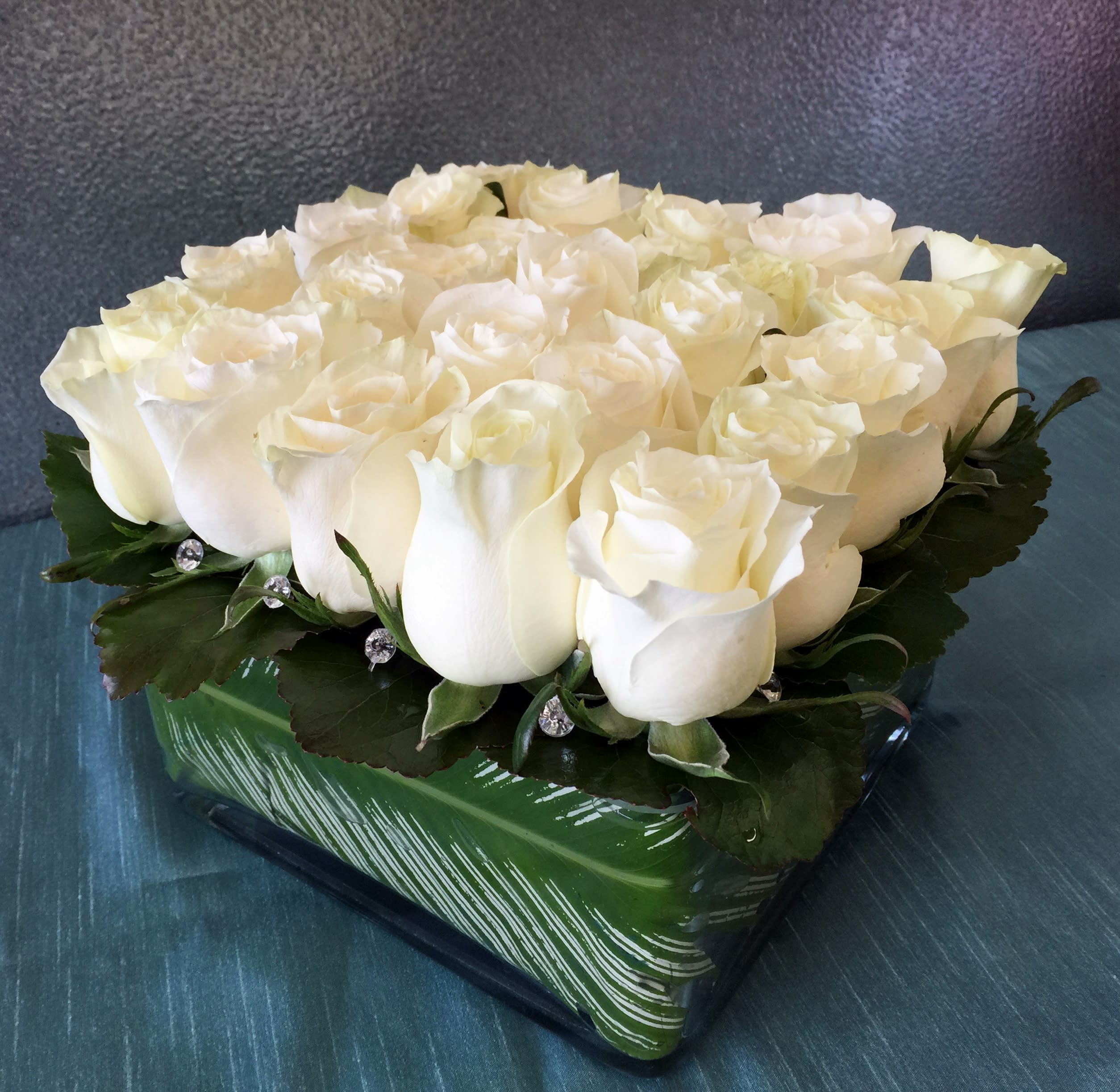 White rose arrangement in a green square vase