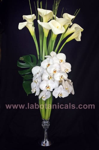 White calla lilies and orchids arranged in a tall glass vase