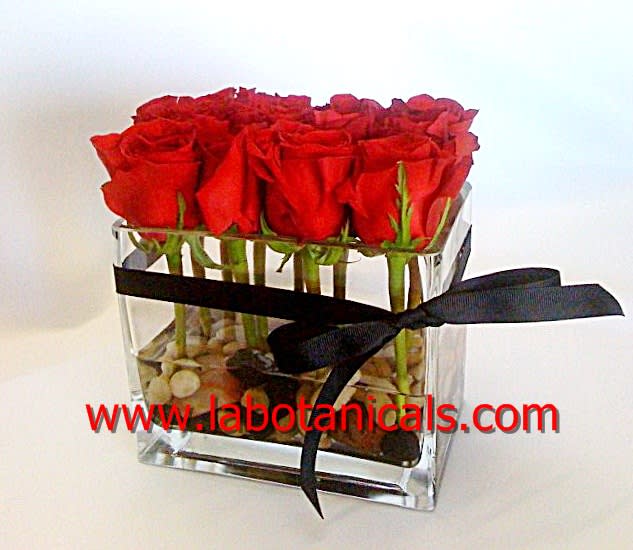 Red roses arranged in a clear square vase with a black ribbon