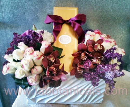 Two floral bouquets flank a gold gift box with a purple ribbon