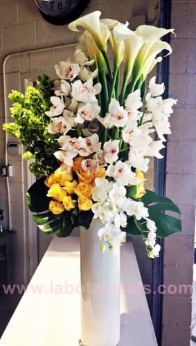 Tall floral arrangement with white calla lilies, orchids, and yellow roses in a white vase